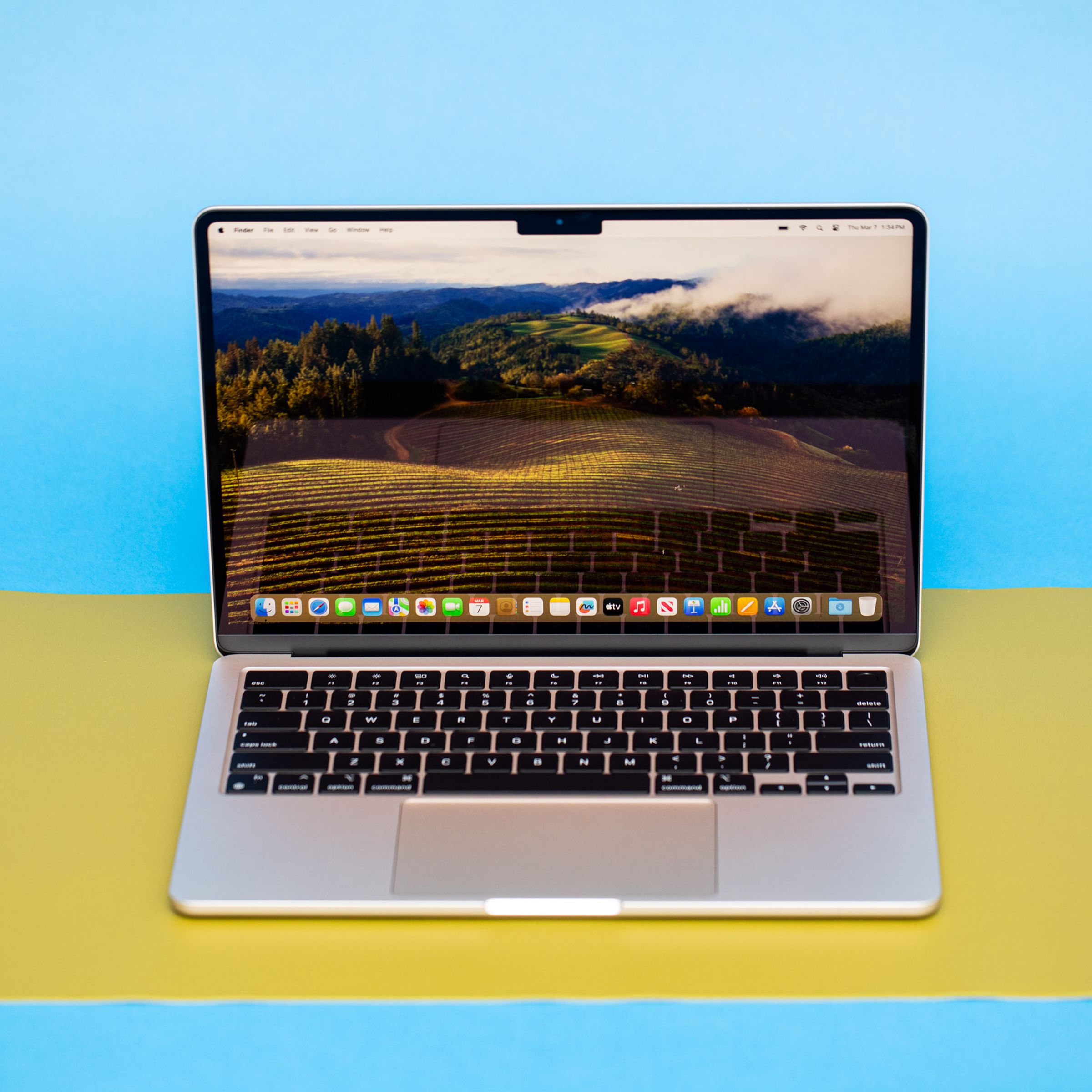 An open and powered on laptop against a blue background sitting on top of a bright yellow mat.