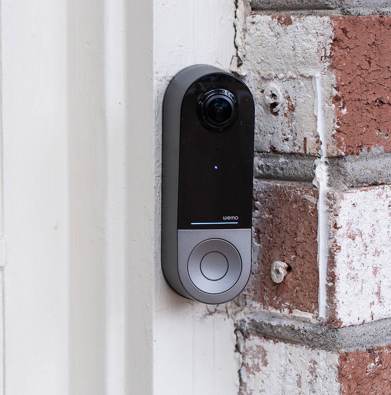 A black and silver doorbell with a camera on a brick wall.