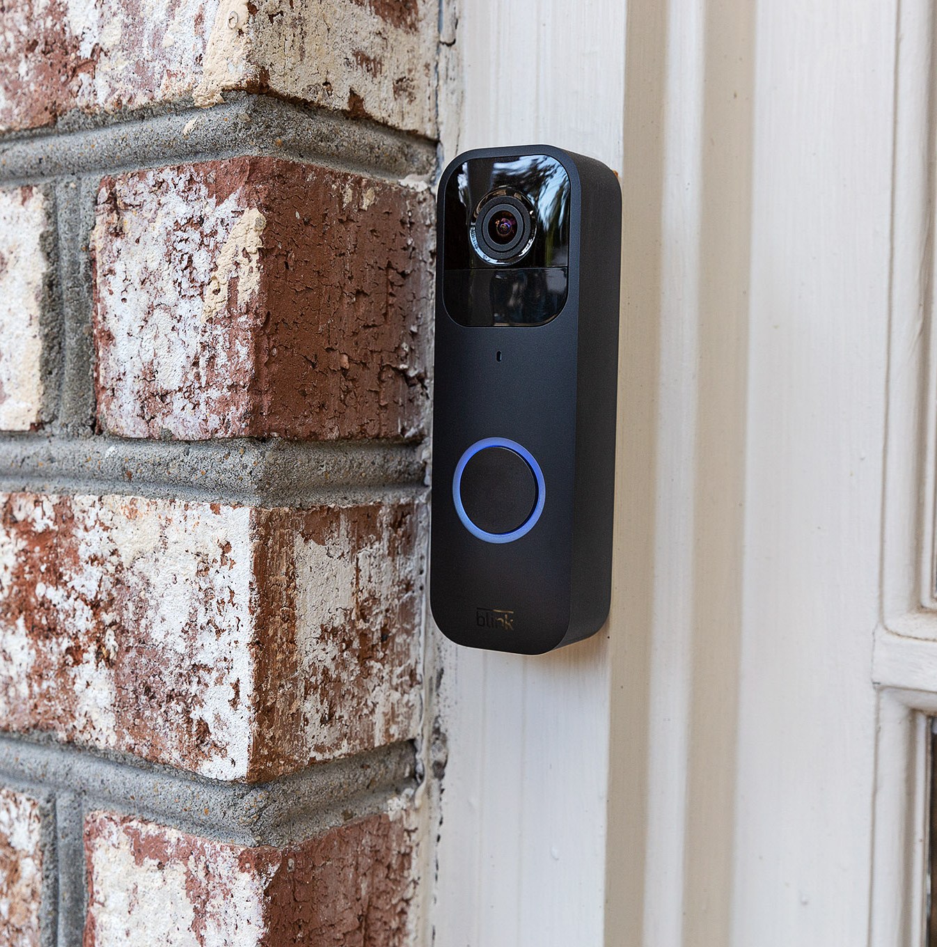 The black Blink Video Doorbell hung up on a brick wall outside of a house.