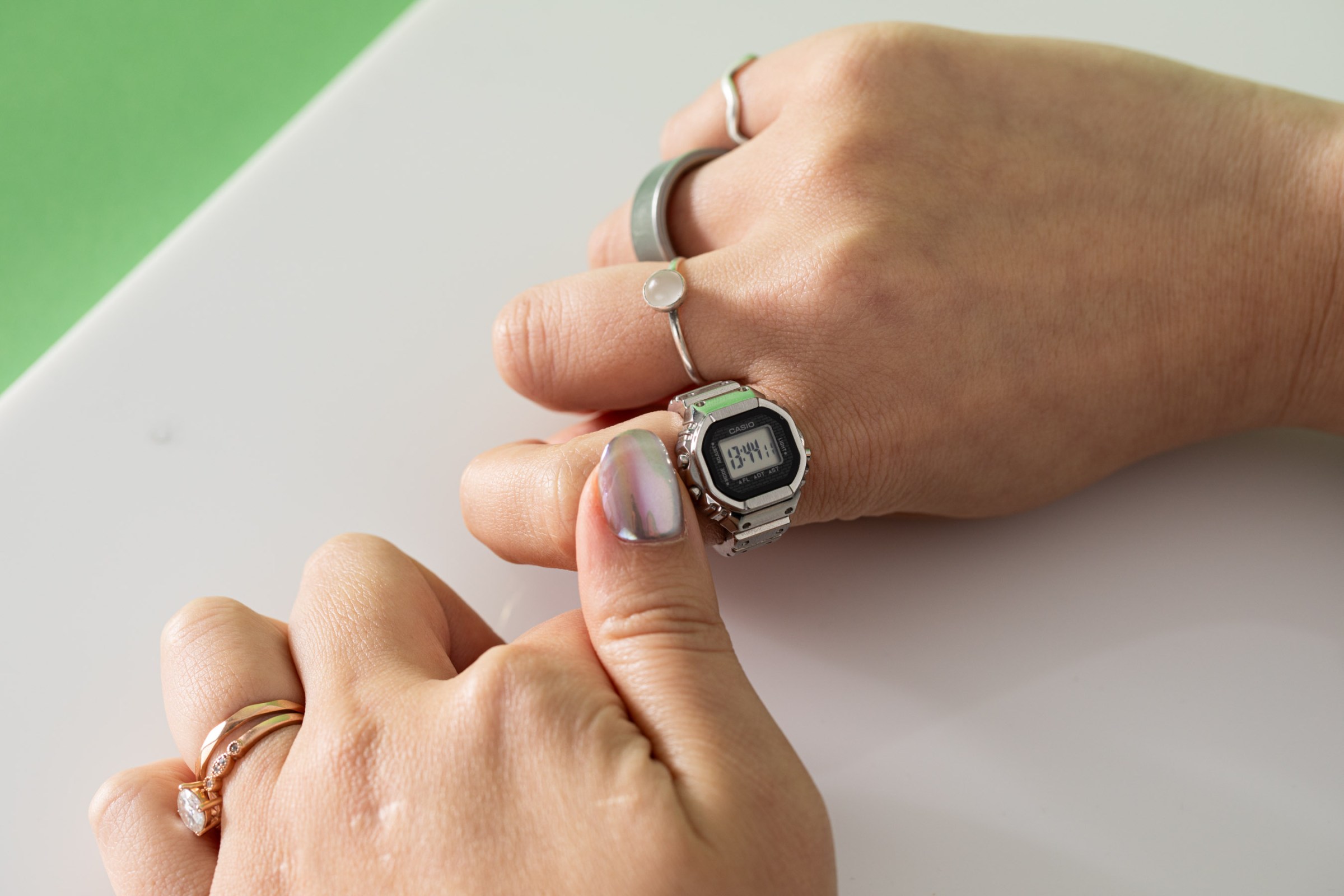 Photo of Senior Reviewer Victoria Song trying to use the buttons on the Casio Ring Watch with her thumb. There’s a white and green background, and it’s clear that it’s awkward to press the button.