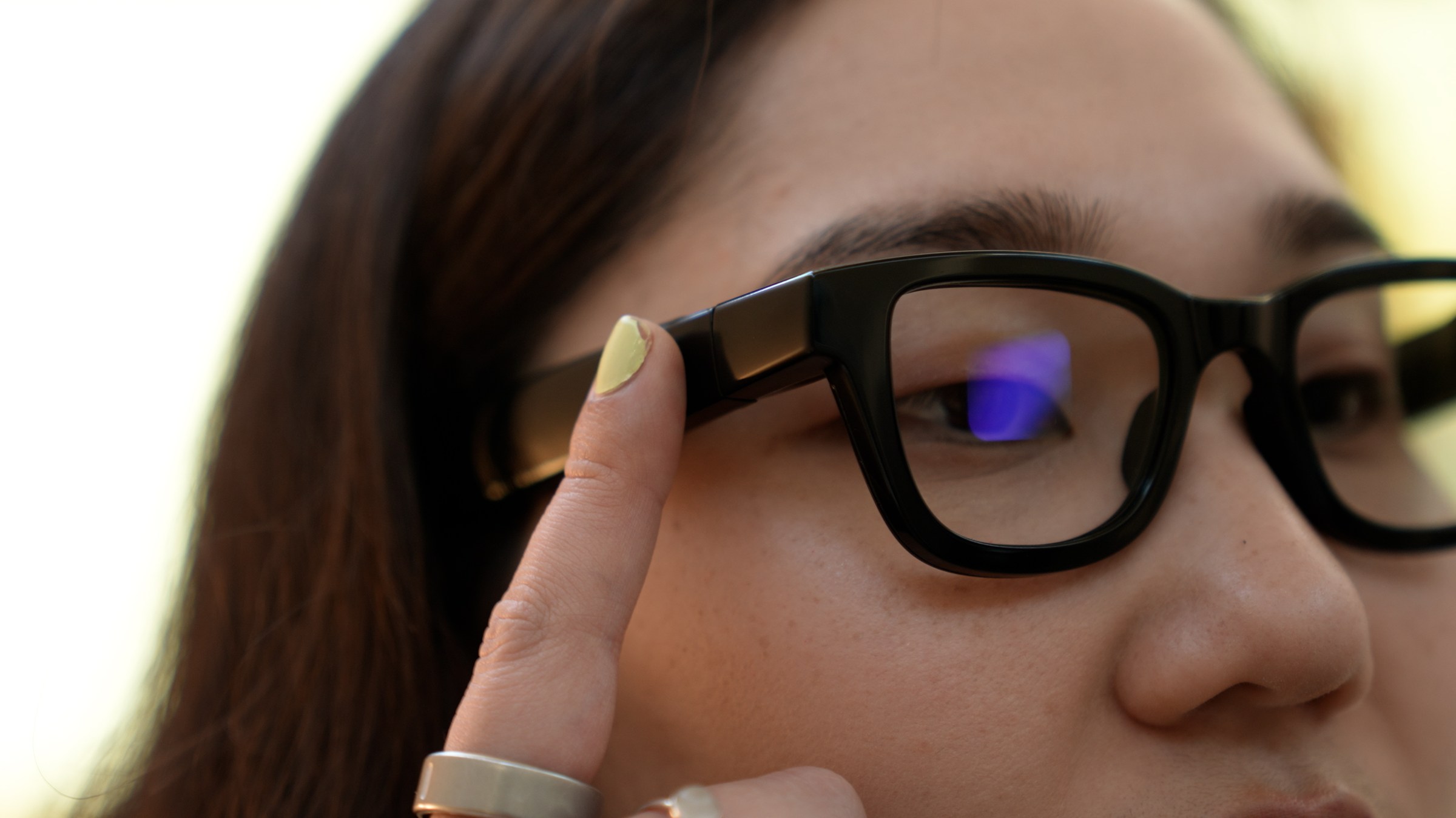 Closeup of senior reviewer Victoria Song tapping the side of the Android XR prototype glasses to bring up Gemini.