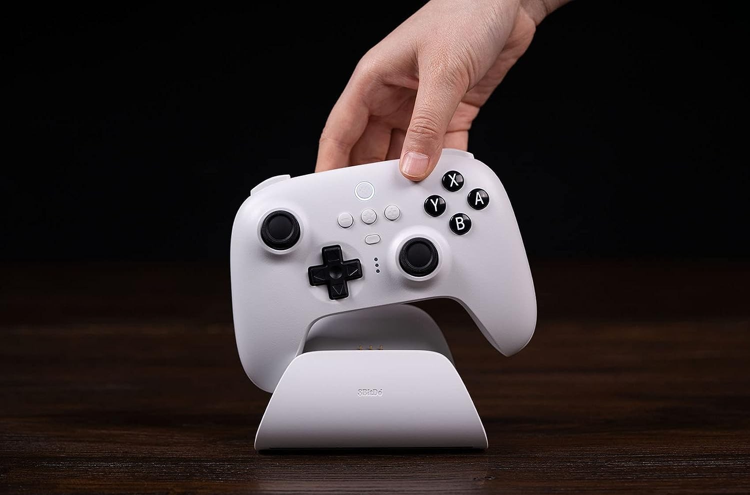 A hand picking up the white 8BitDo Ultimate Bluetooth Controller from its charging cradle.