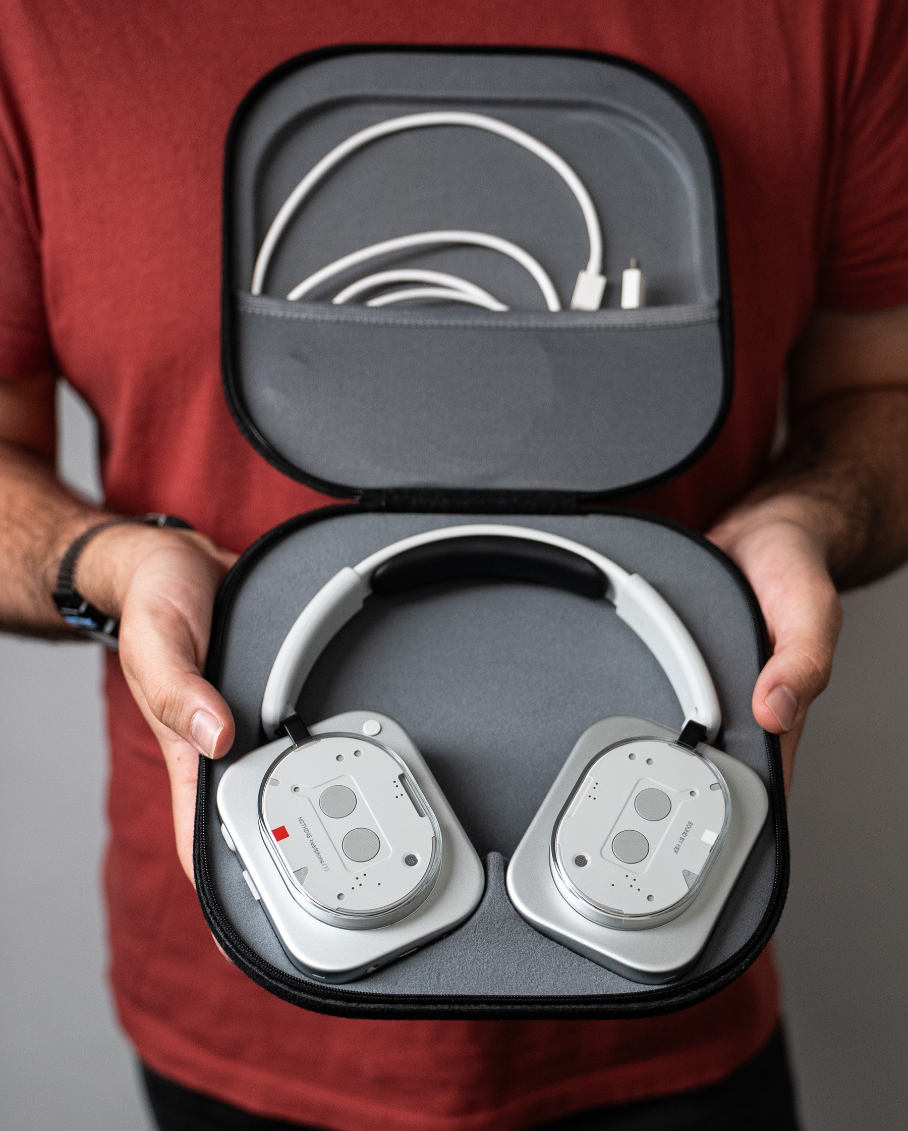 Holding the Nothing Headphones case open with the Nothing Headphone 1 laying flat inside. Two cables are in a little pouch on the top flap of the case.