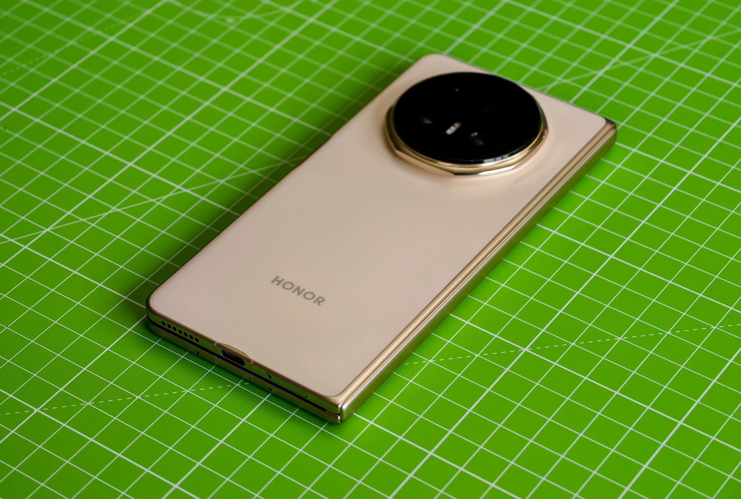 The Honor Magic V5 lying closed on a green cutting mat, with the camera facing up