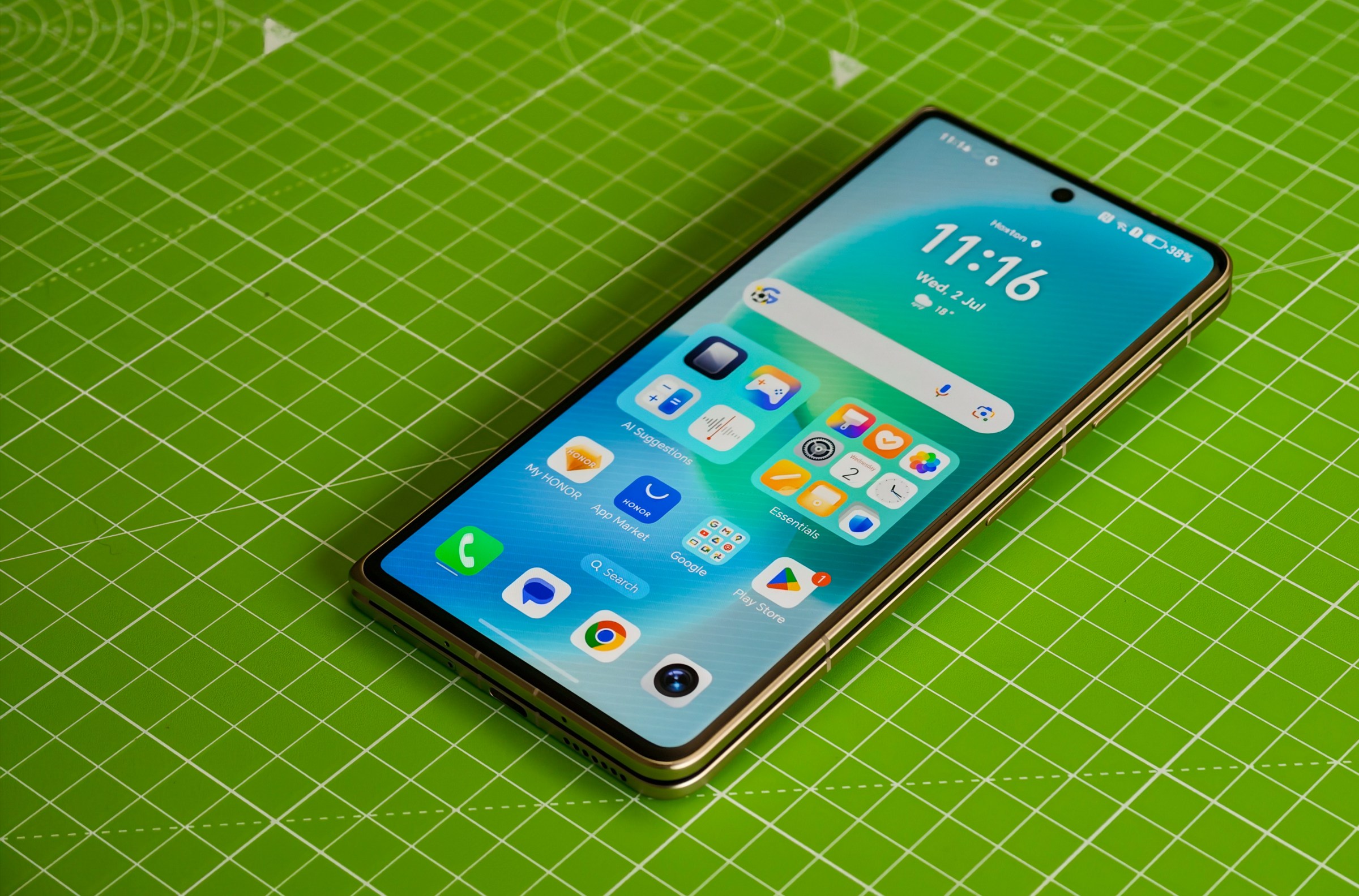 The Honor Magic V5 lying closed on a green cutting mat, showing the homescreen