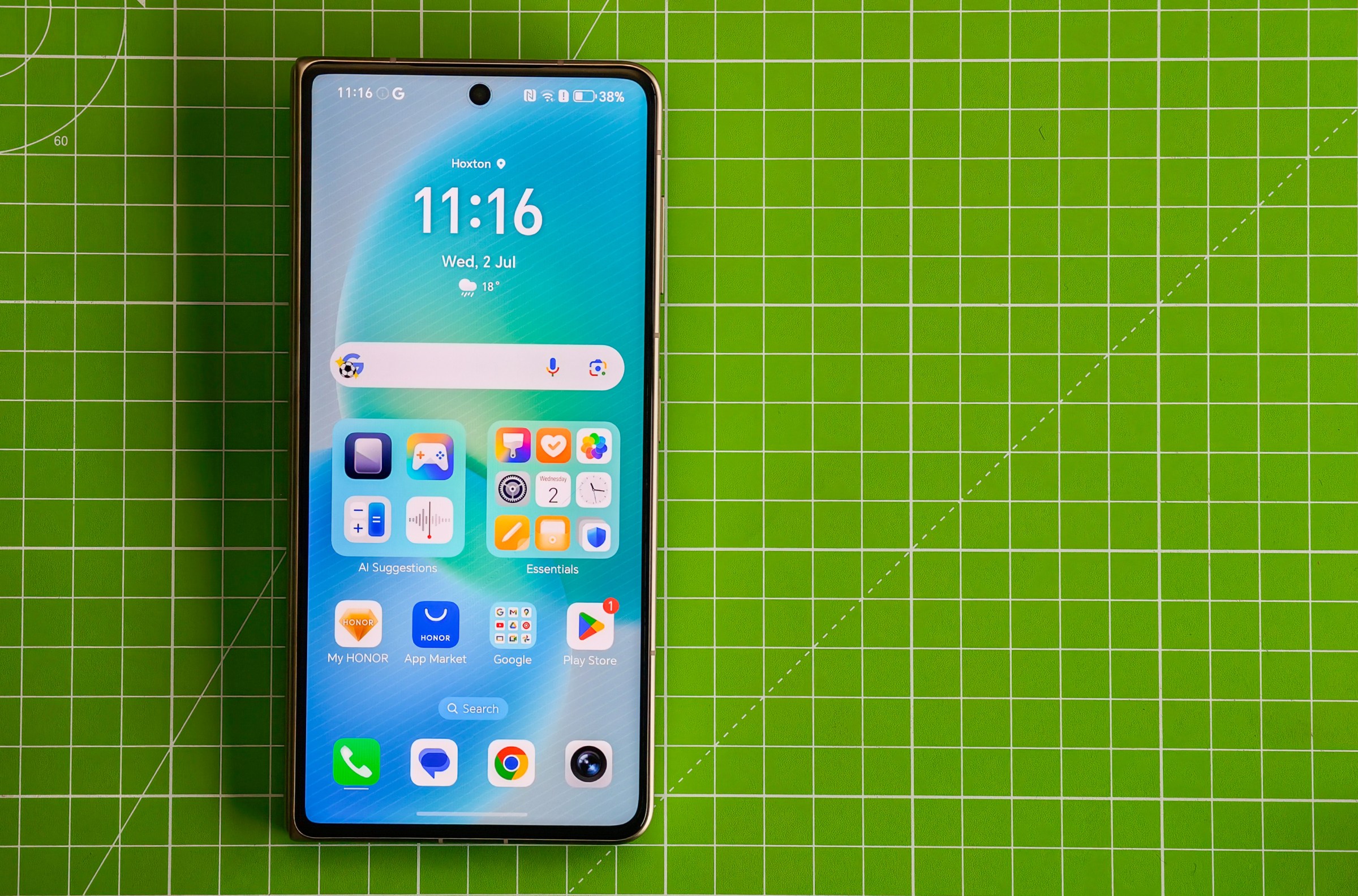 The Honor Magic V5 lying closed on a green cutting mat, showing the homescreen