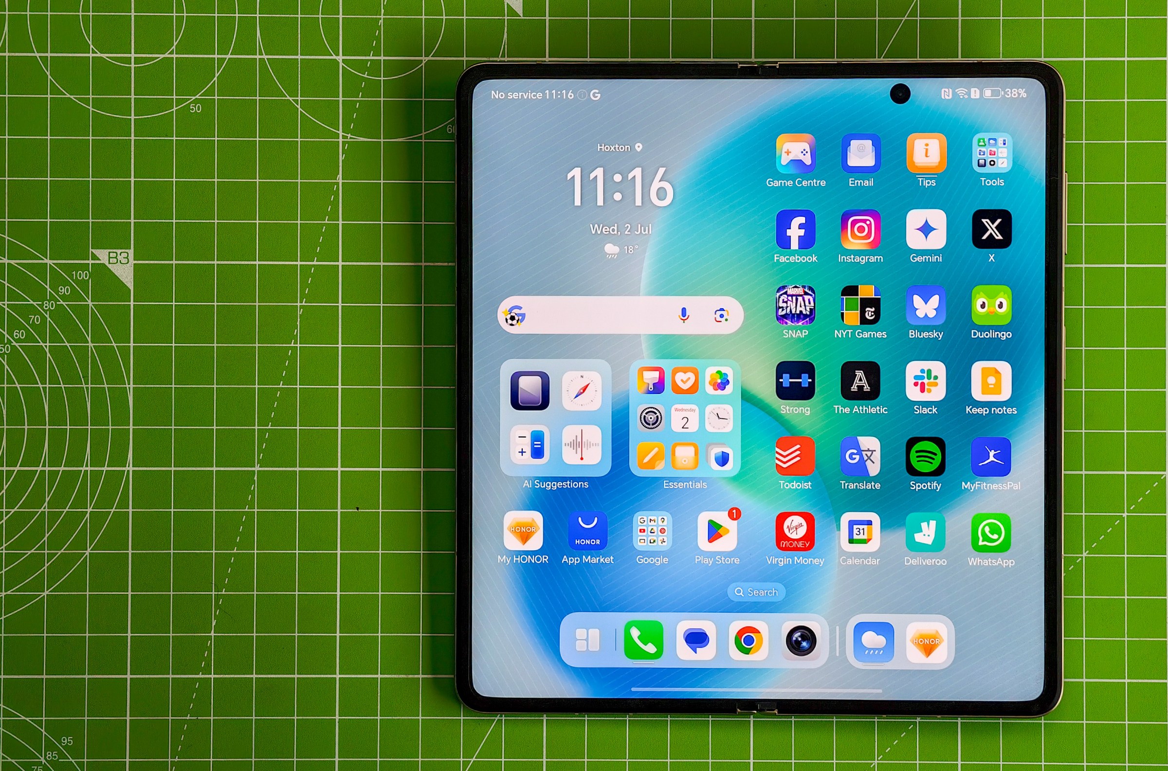 The Honor Magic V5 lying open on a green cutting mat, showing the homescreen