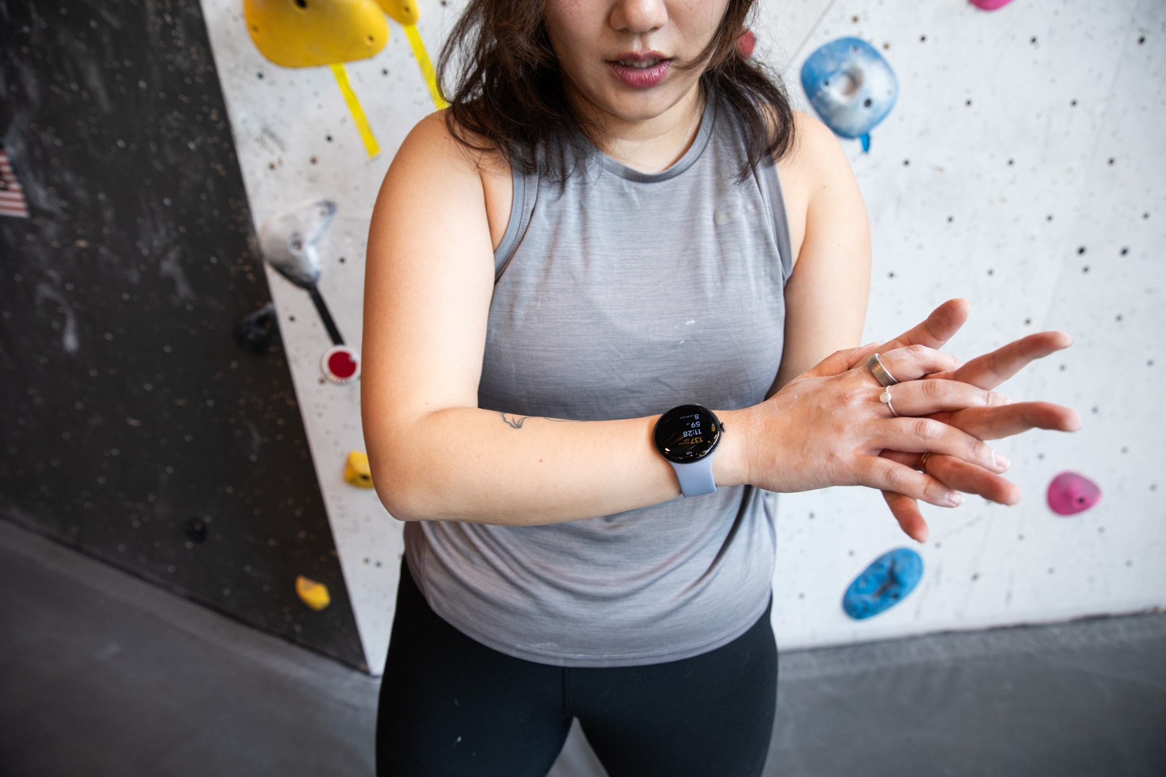 Someone wearing the Pixel Watch 4 chalking up their hands while standing in front of a colorful rock climbing wall.