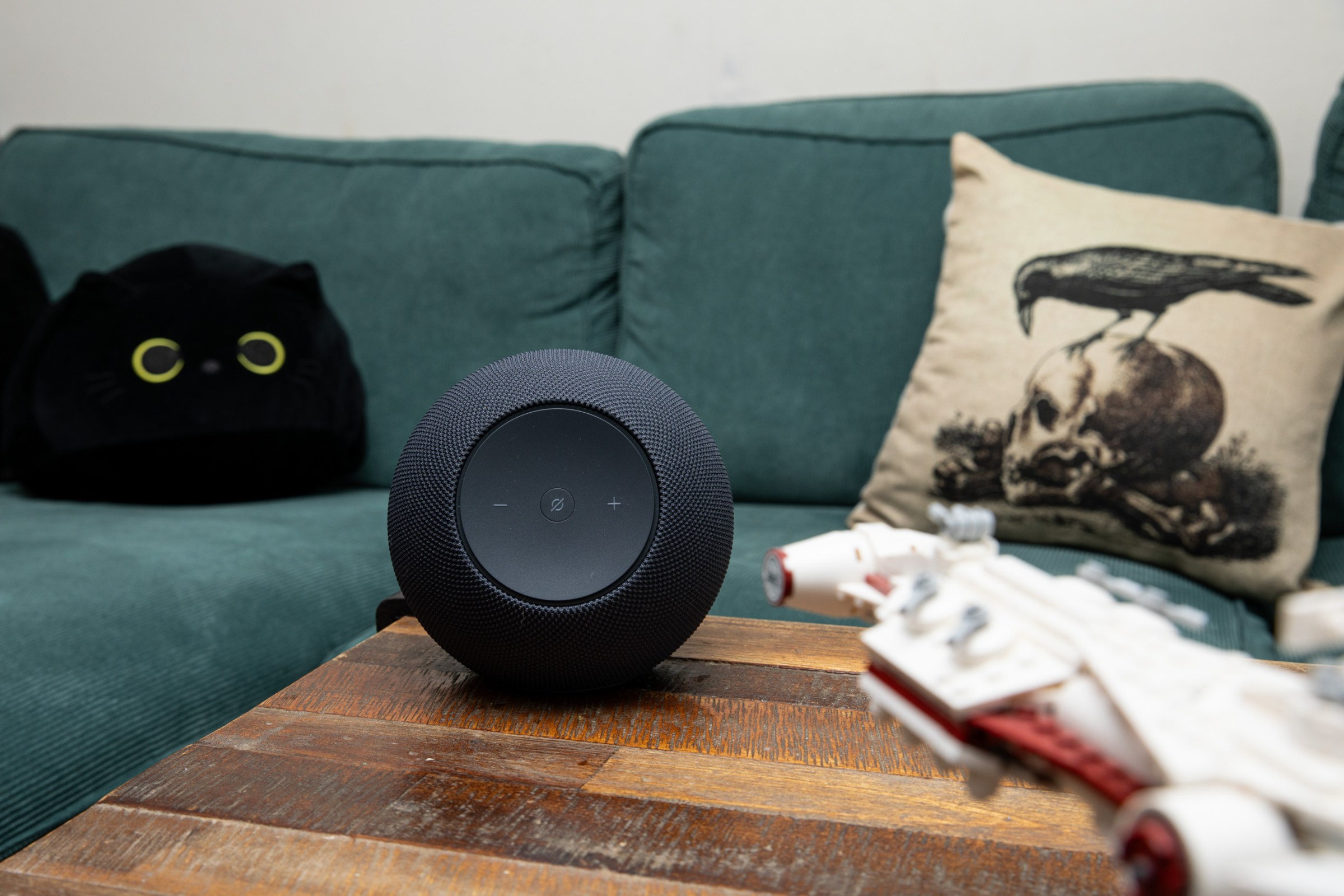 The Amazon Echo Studio on a wooden coffee table in front of a green couch with a Lego Star Wars ship in the foreground.