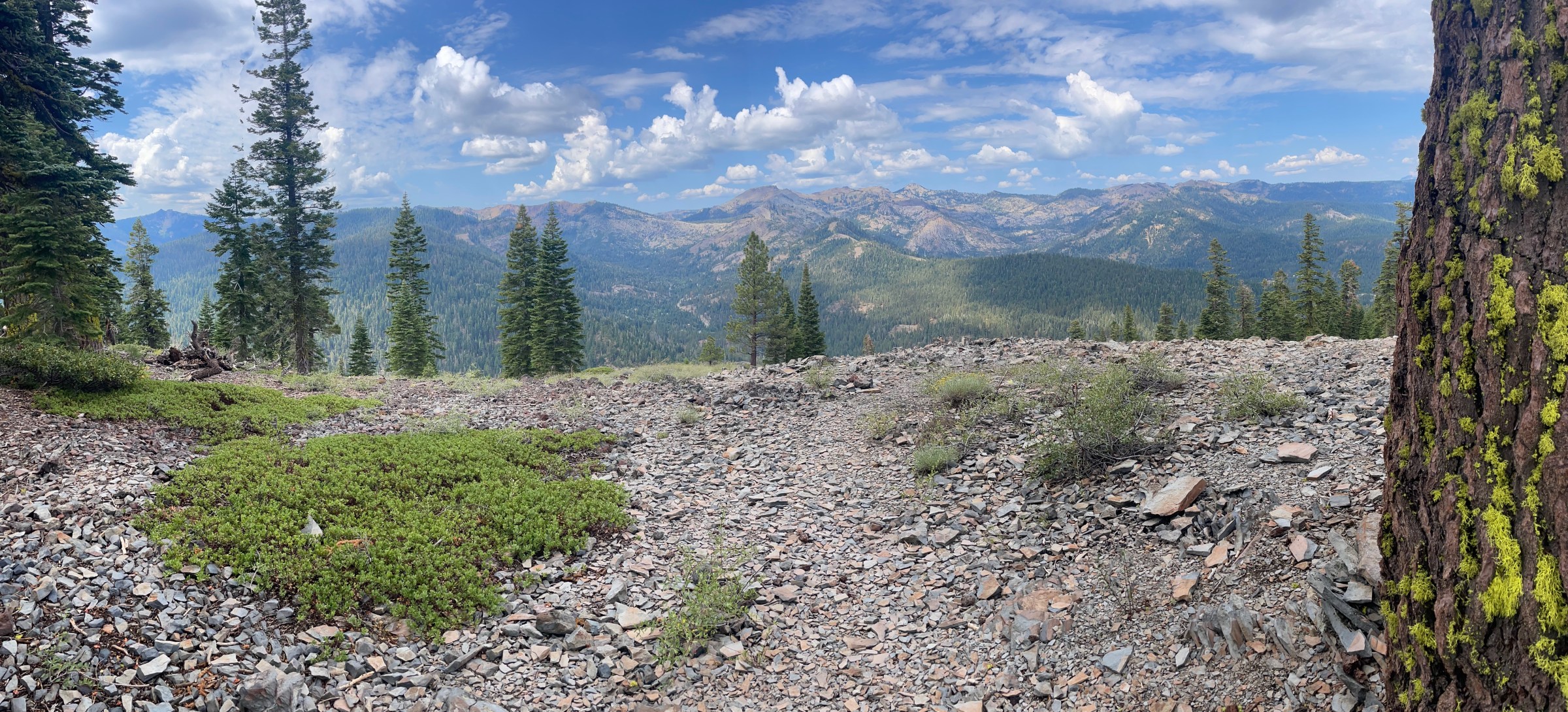 A view of mountains, from a trail covered in scree, with a gorgeous blue sky and little fluffy clouds.