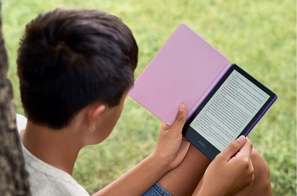 Someone outside sitting in grass and reading on a Kindle Paperwhite Kids device