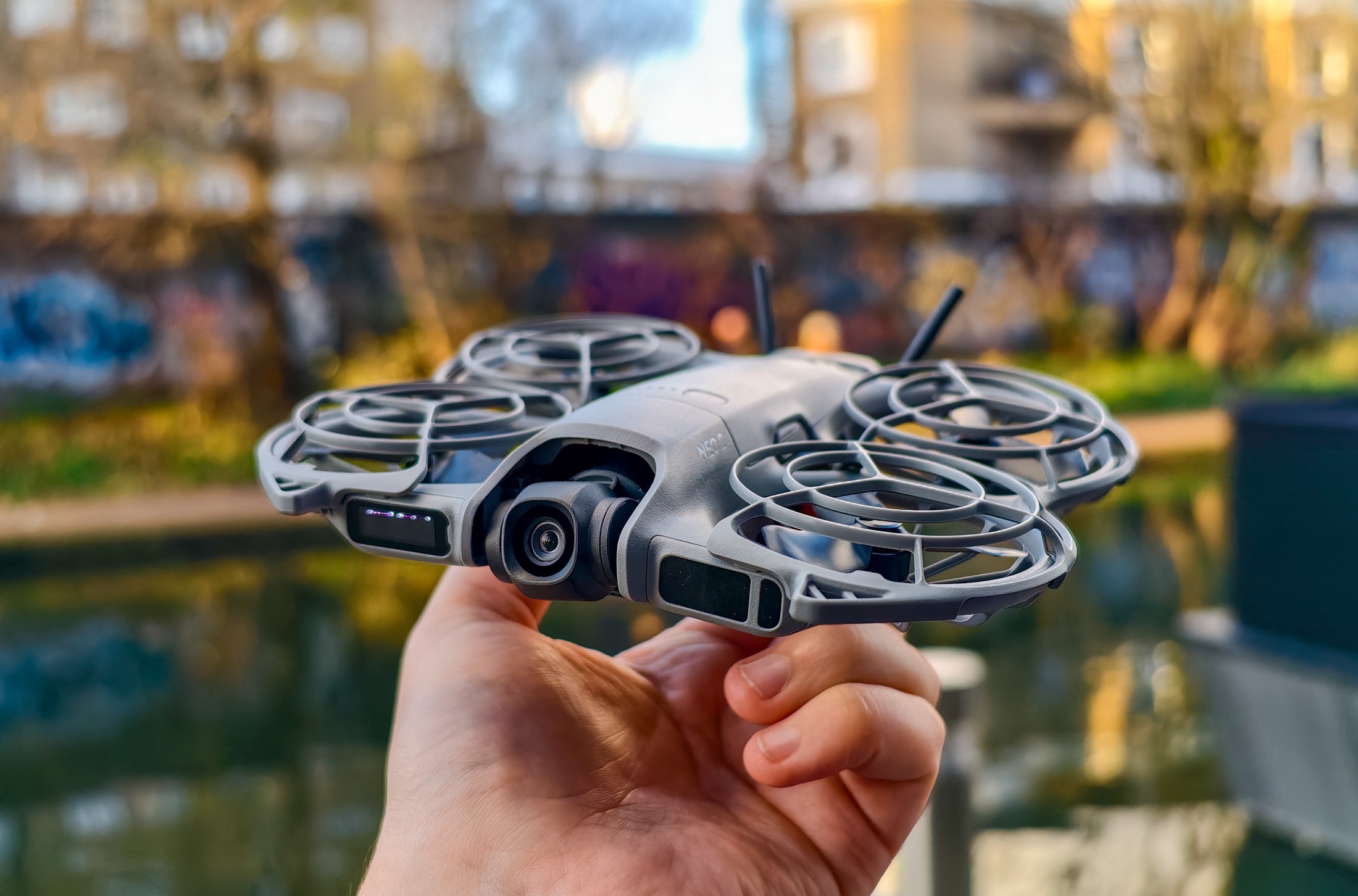 Photo of DJI Neo 2 held in a hand in front of a canal