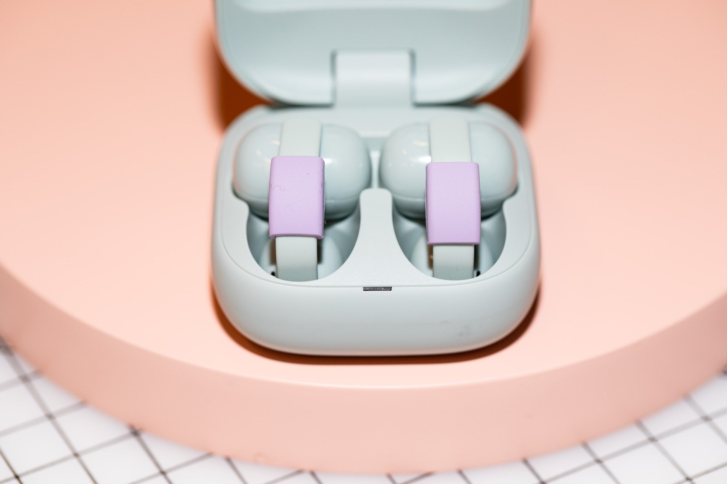 The Sony LinkBuds Clip earbuds in their open charging case on a peach surface.