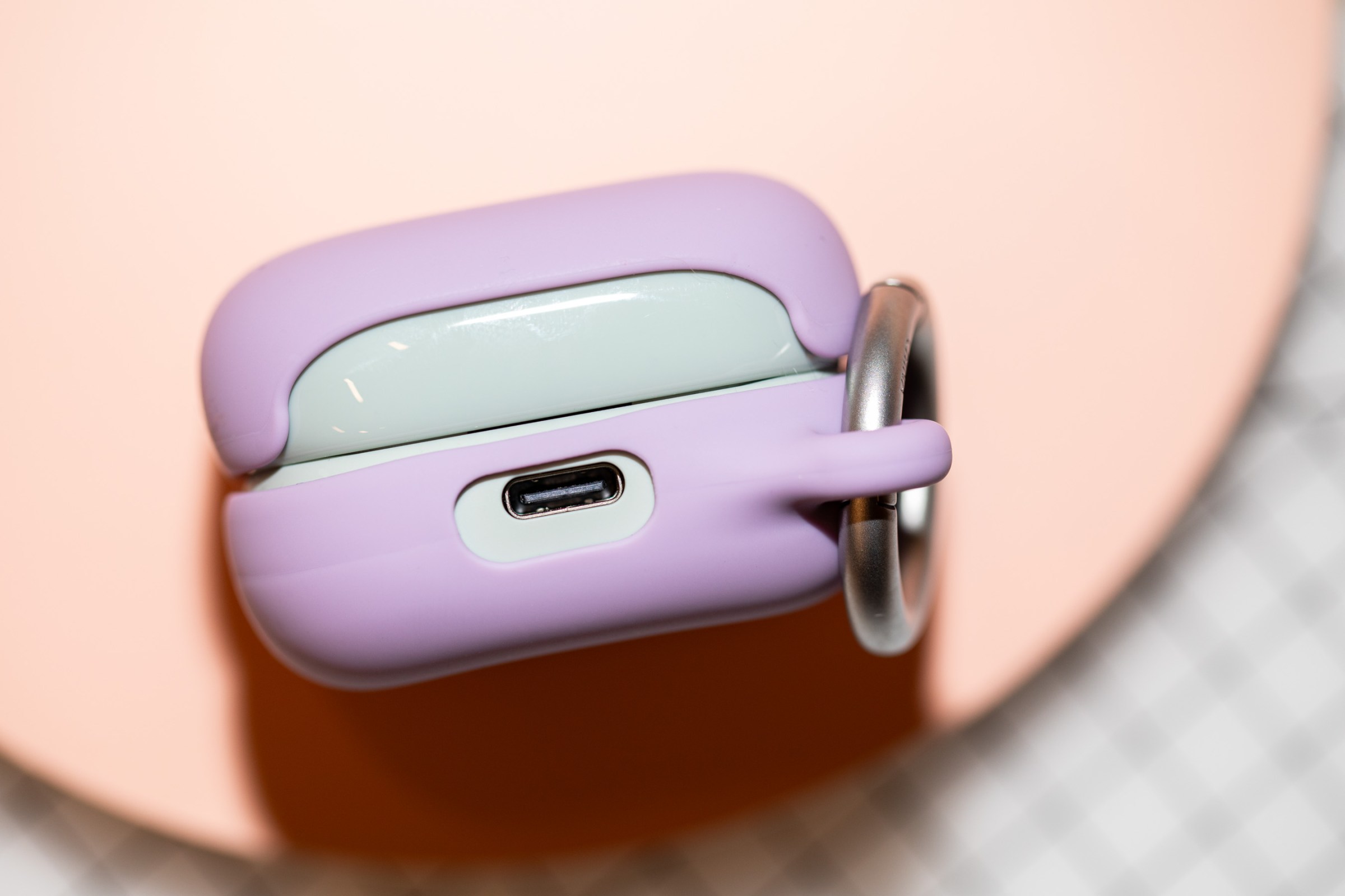 The USB-C charging port of the Sony LinkBuds Clip case in green with a lavender cover on a peach surface.