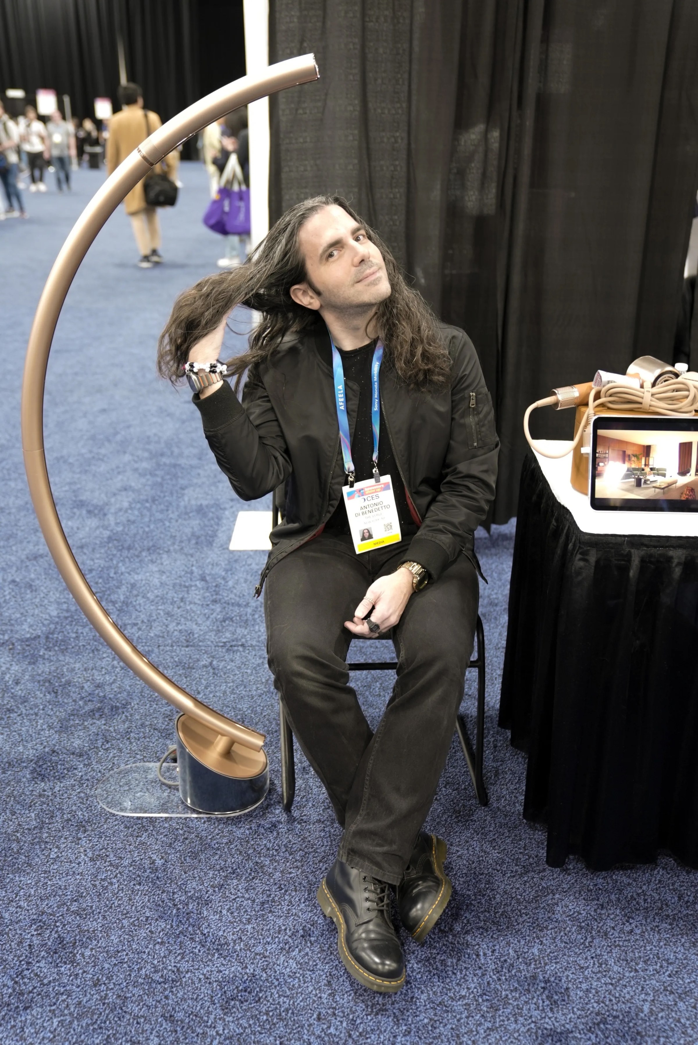 a long-haired man underneath a floor lamp that is also a hair dryer
