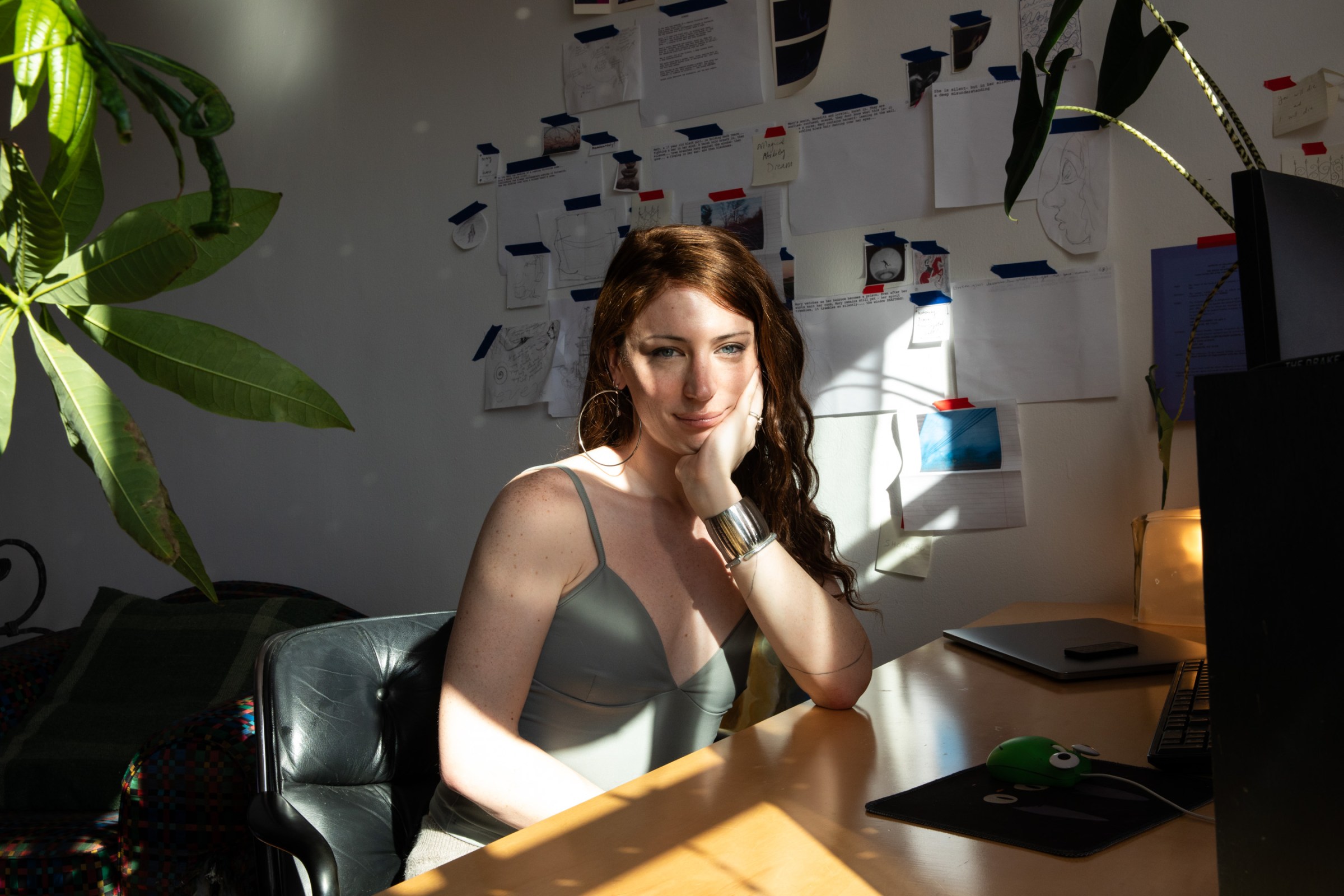 Bree sits at her desk with papers and sketches behind her on the wall.