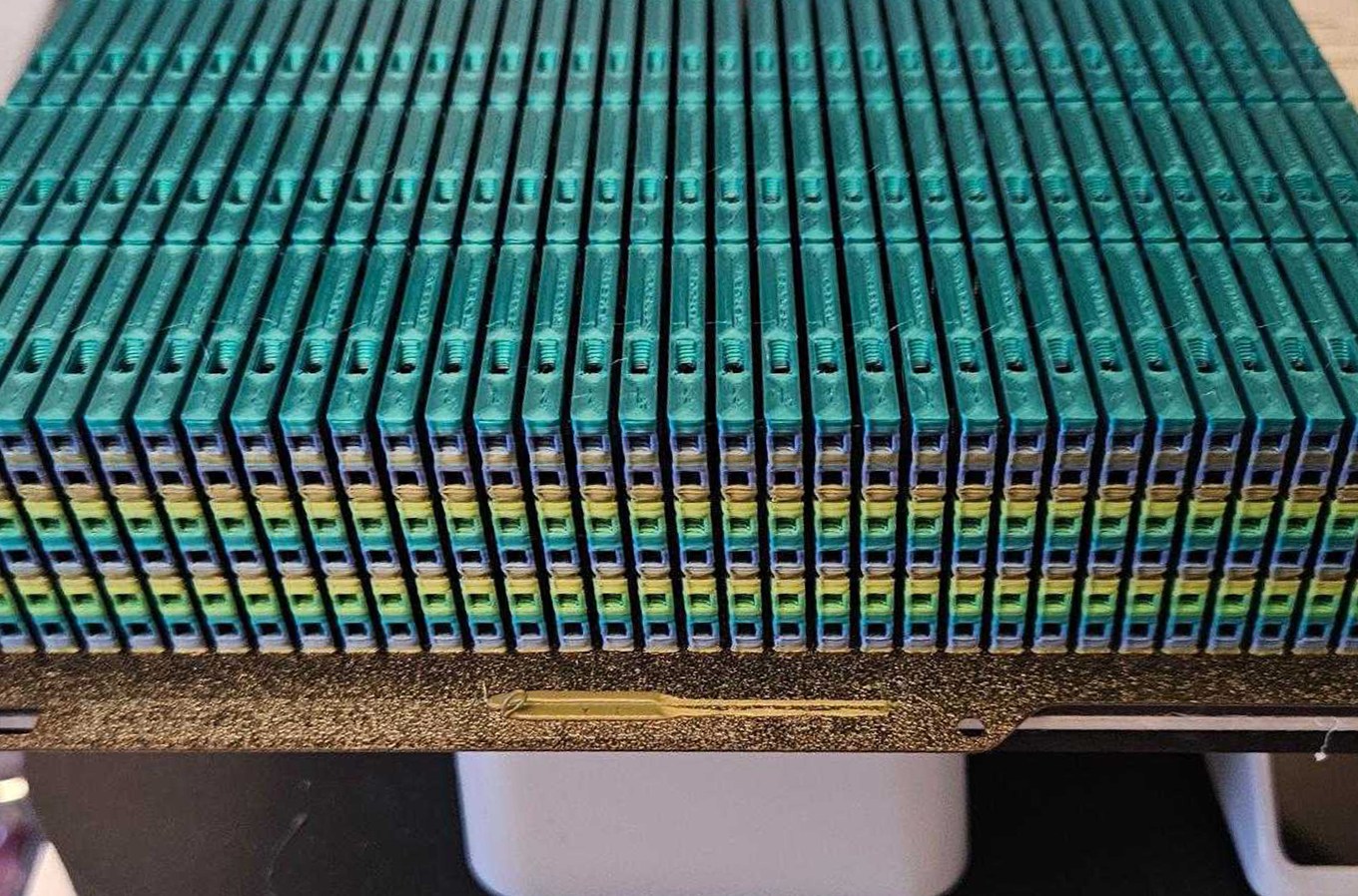 Over 500 rainbow whistles, stacked three high, sit atop the bed of a tiny Bambu A1 Mini printer. They were all printed at once.