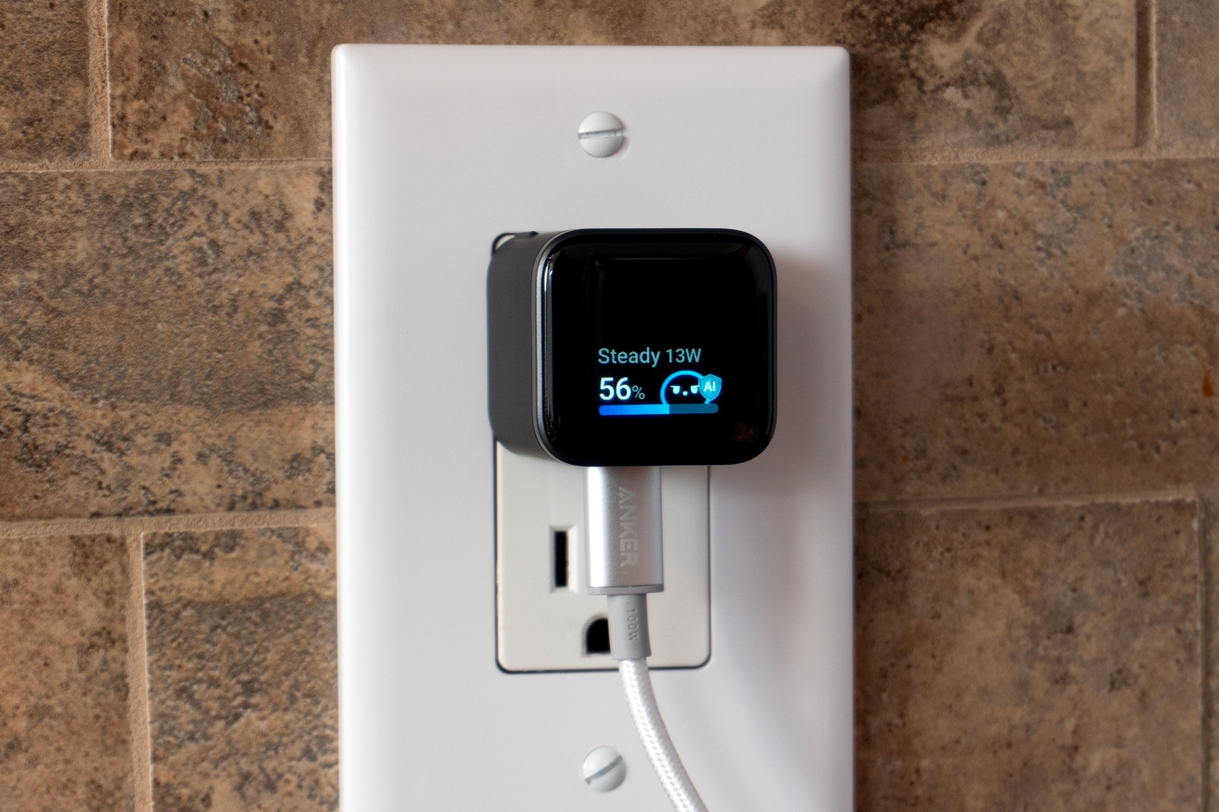 The Anker Nano charger plugged into a wall outlet with its screen flipped so the USB-C port is on the bottom.