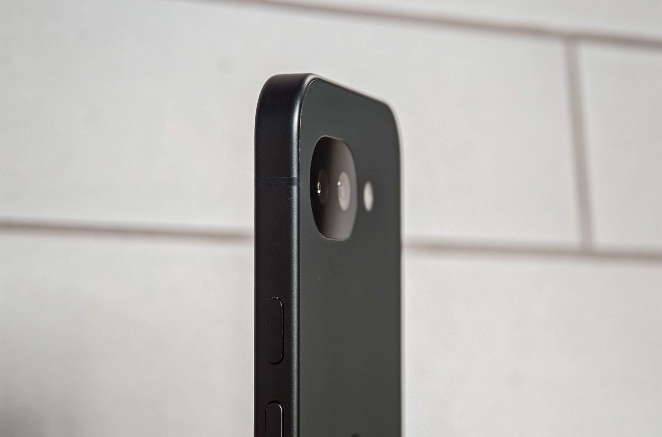 Photo of Google Pixel 10A in front of white tiles, showing the camera from an angle