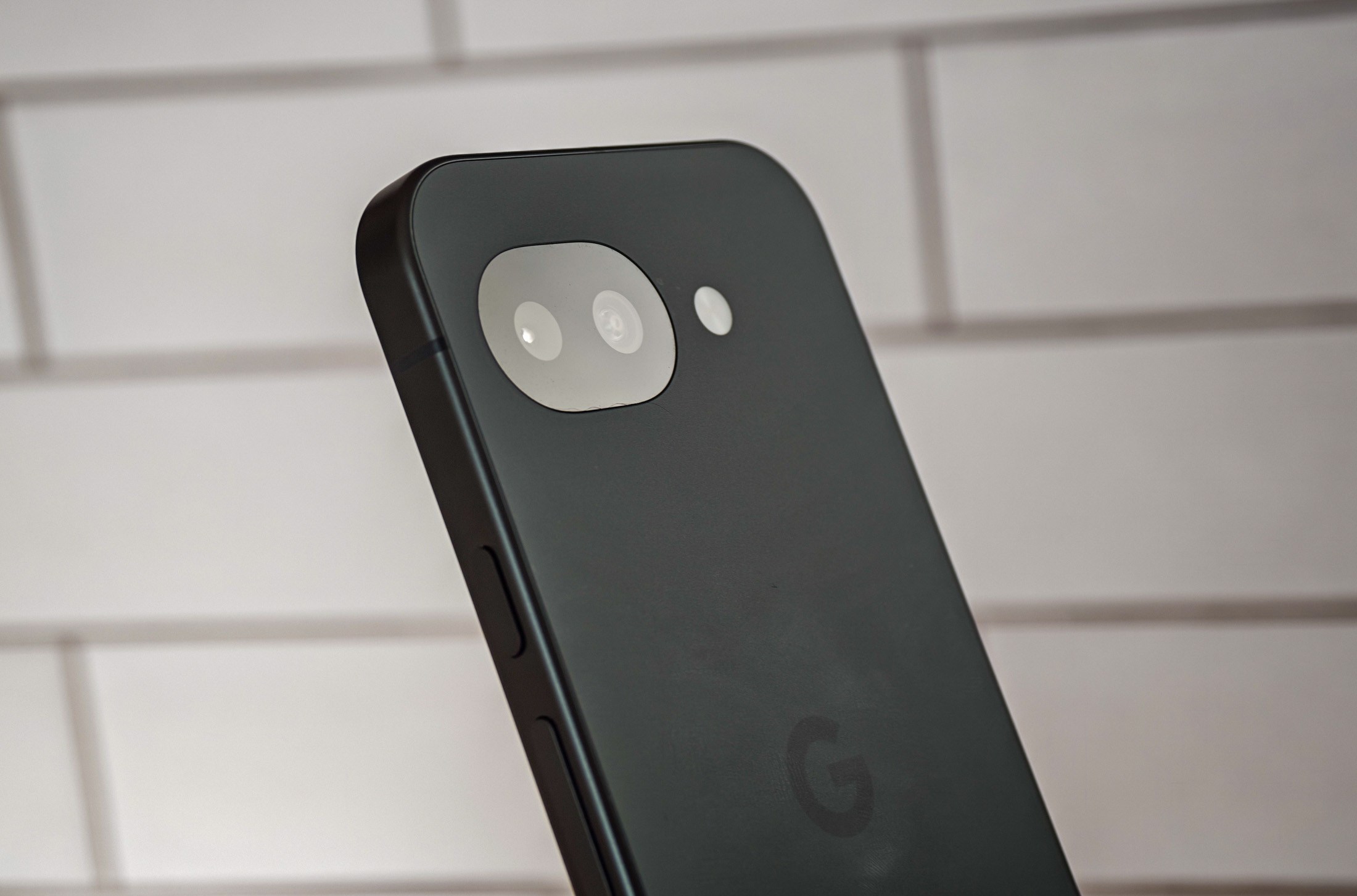 Photo of Google Pixel 10A in front of white tiles, showing the camera from an angle