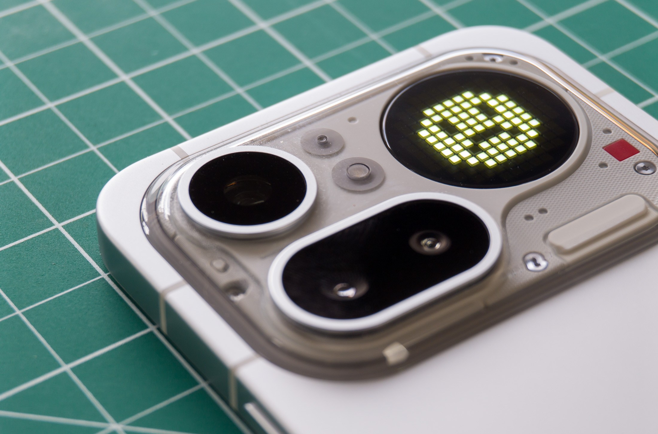 Photo of Nothing Phone 4A Pro on a green cutting mat showing the camera module with an unhappy smiley face on the Glyph Matrix