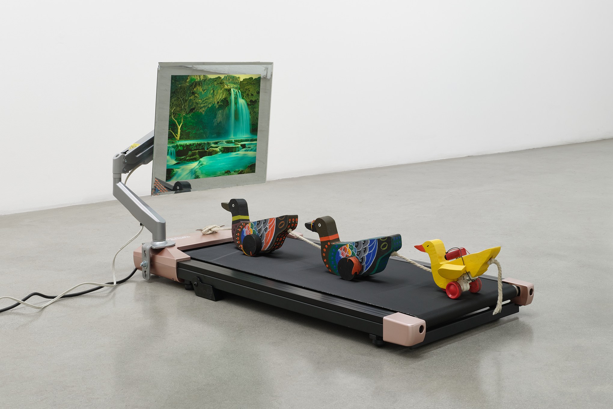 Toy wooden ducks on a treadmill facing a moving waterfall picture frame.