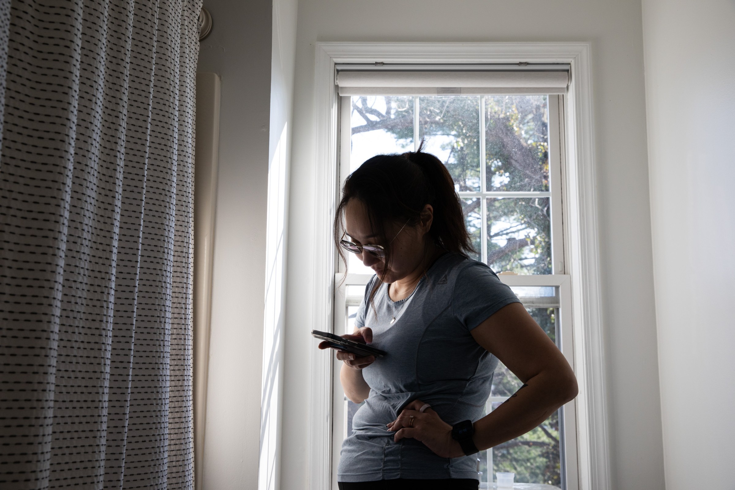 Senior reviewer Victoria Song looking down at a CGM phone app in a bathroom while standing in front of a window