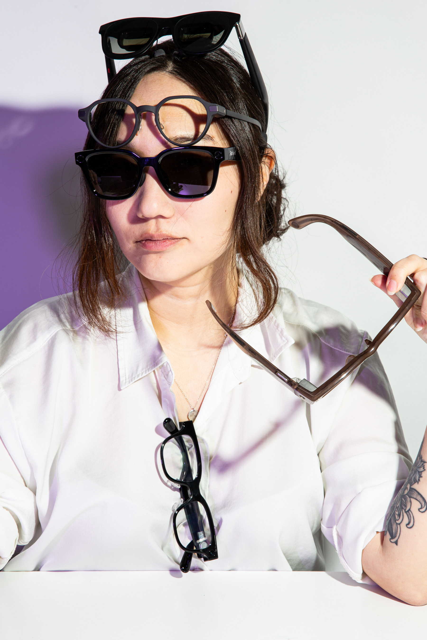 Senior reviewer Victoria Song posing while wearing a sunglasses type of smart glasses, with three others on her body and one being held jauntily in her hand.