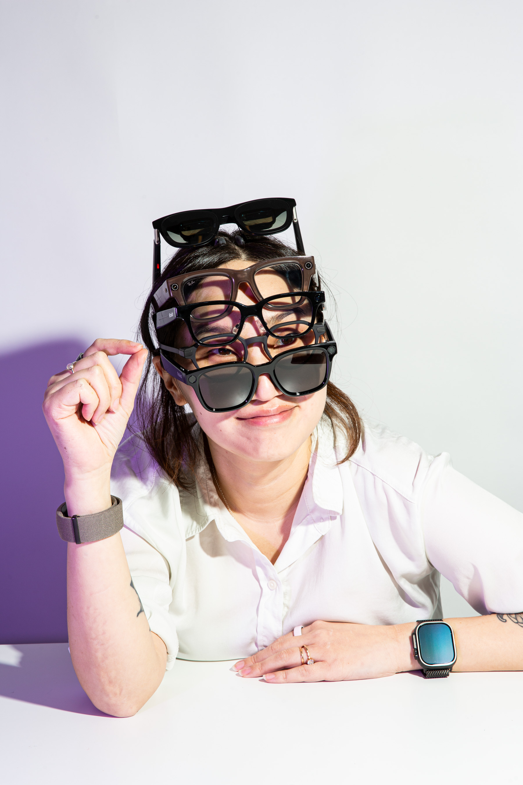 Senior reviewer Victoria Song with a pained smile and dead eyes, wearing five smart glasses simultaneously stacked on her head while making a pinching gesture.