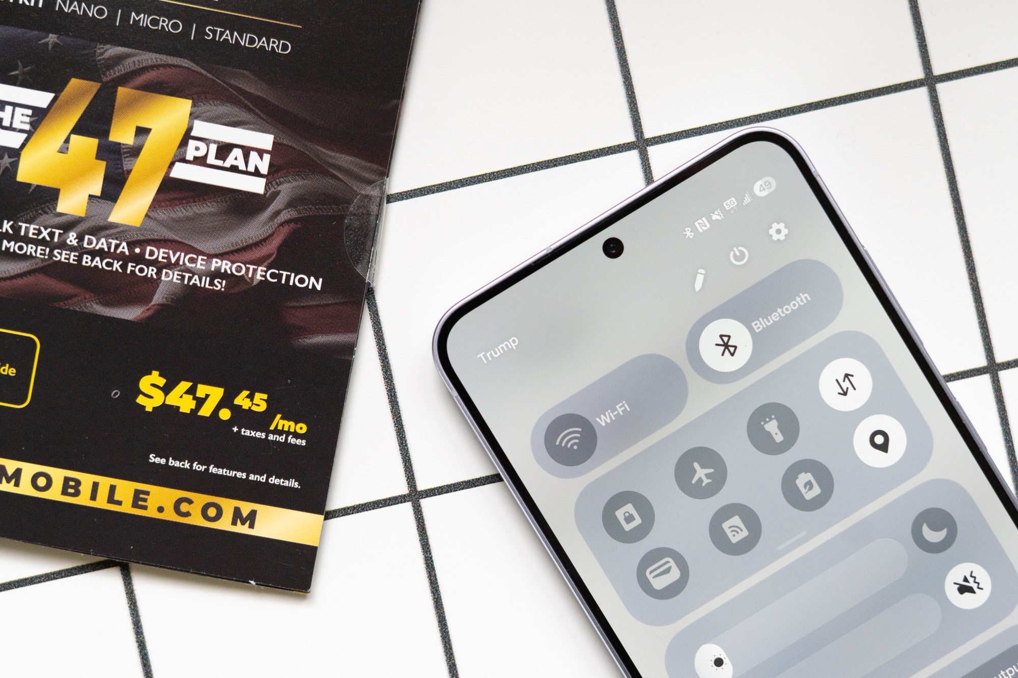 Trump Mobile SIM kit next to a phone showing Trump wireless network indicator in top corner of screen