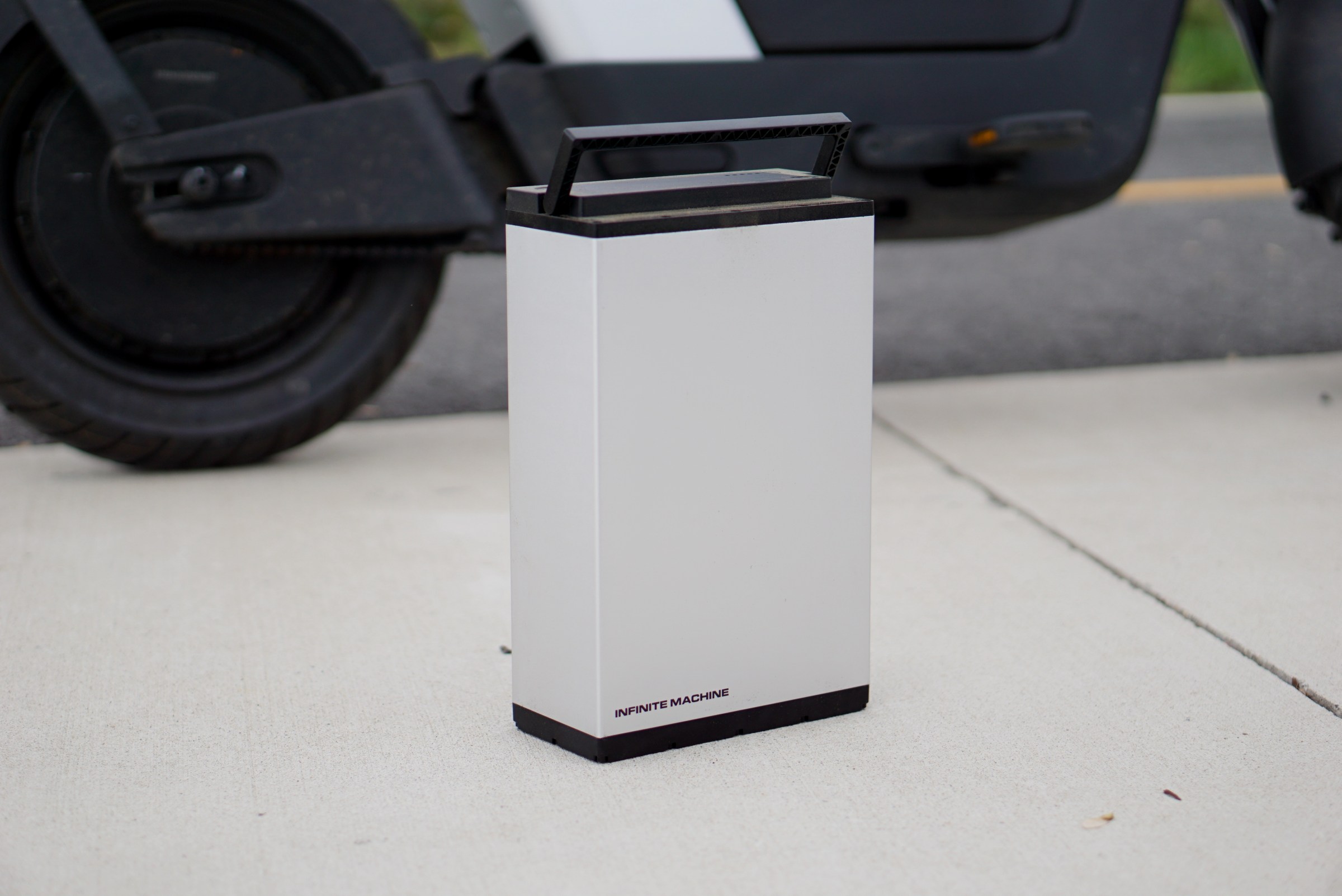 A photo of a large silver battery, on the ground in front of a bike.