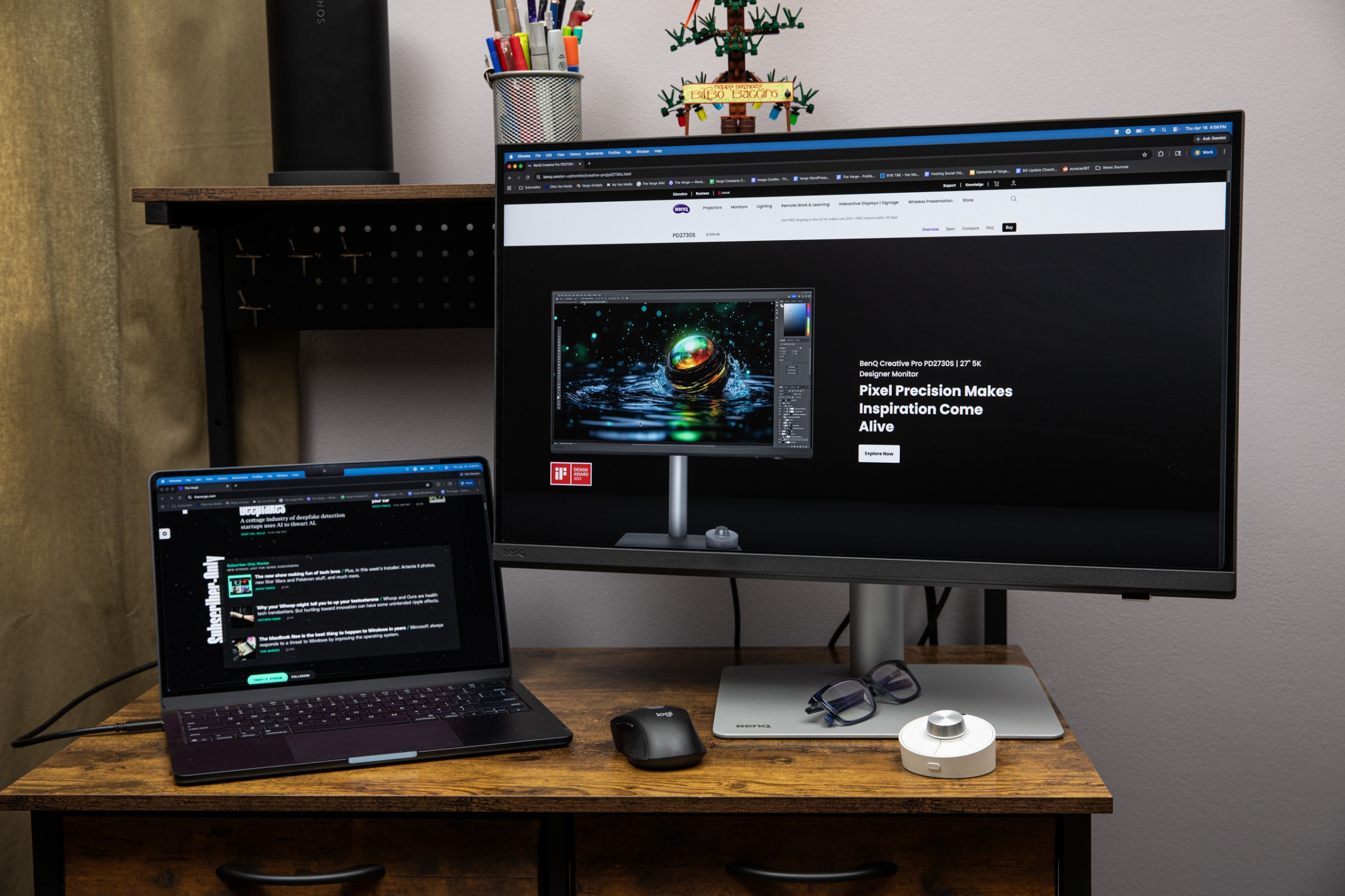 The BenQ PD2730S on a wooden desk with its hotkey puck in front of it while sitting next to a MacBook Air.