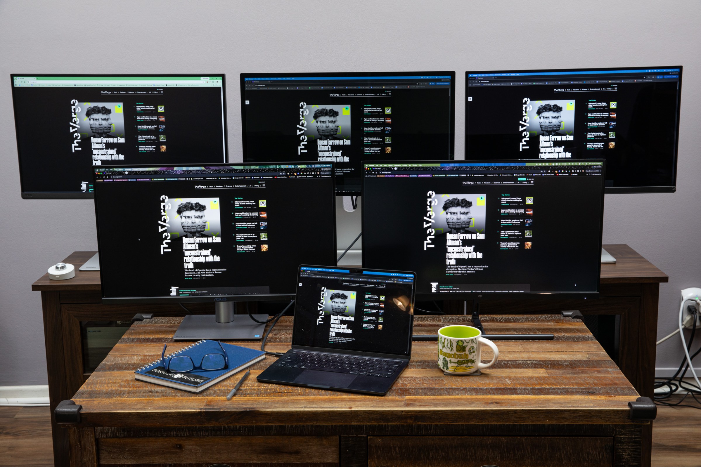 The BenQ PD2730S, Apple Studio Display, BenQ MA270S, Asus ProArt PA27JCV, and KTC H27P3 5K monitors in front of a MacBook Air on a wooden stand and coffee table.