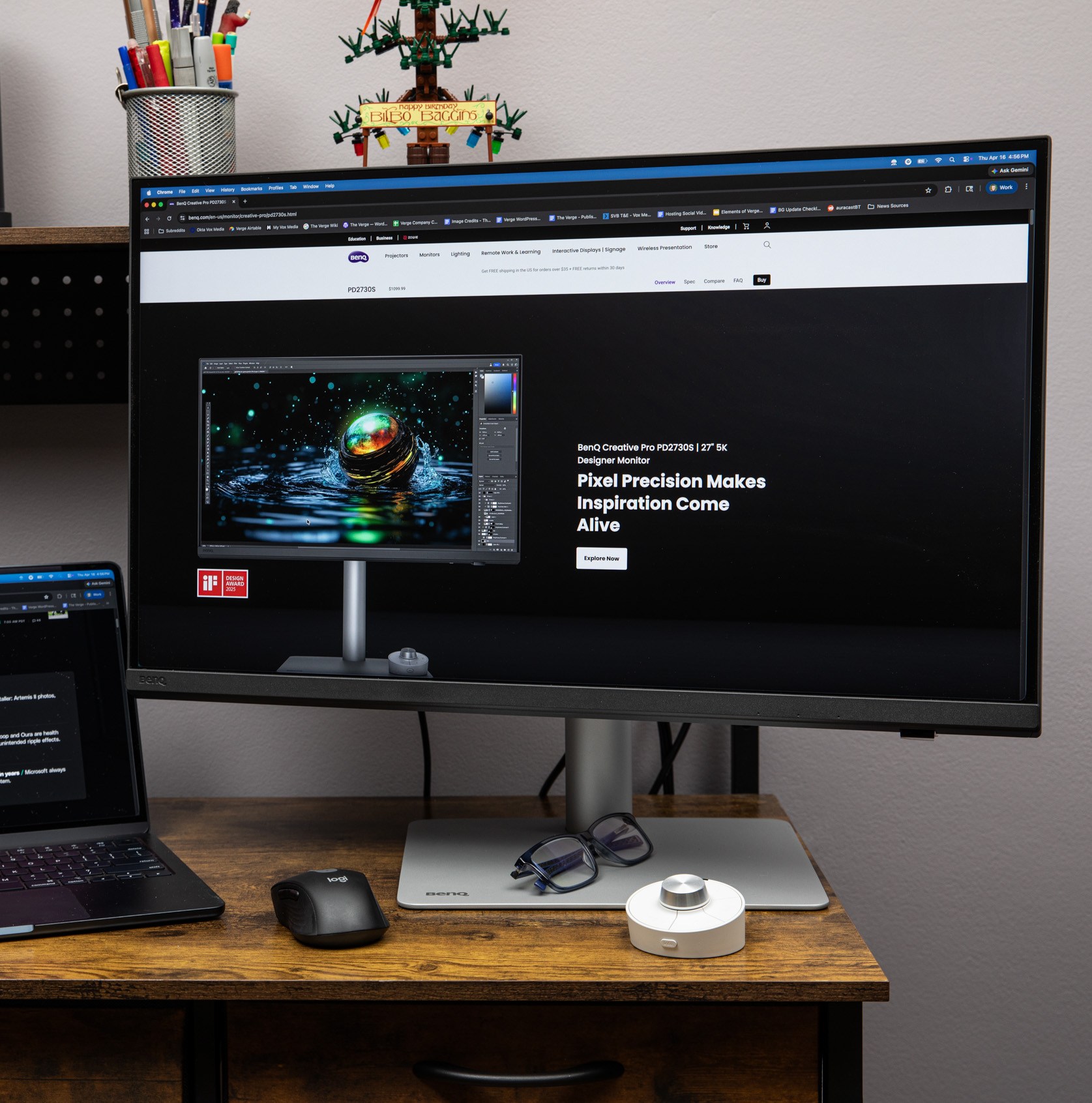 The BenQ PD2730S on a wooden desk with its hotkey puck in front of it while sitting next to a MacBook Air.