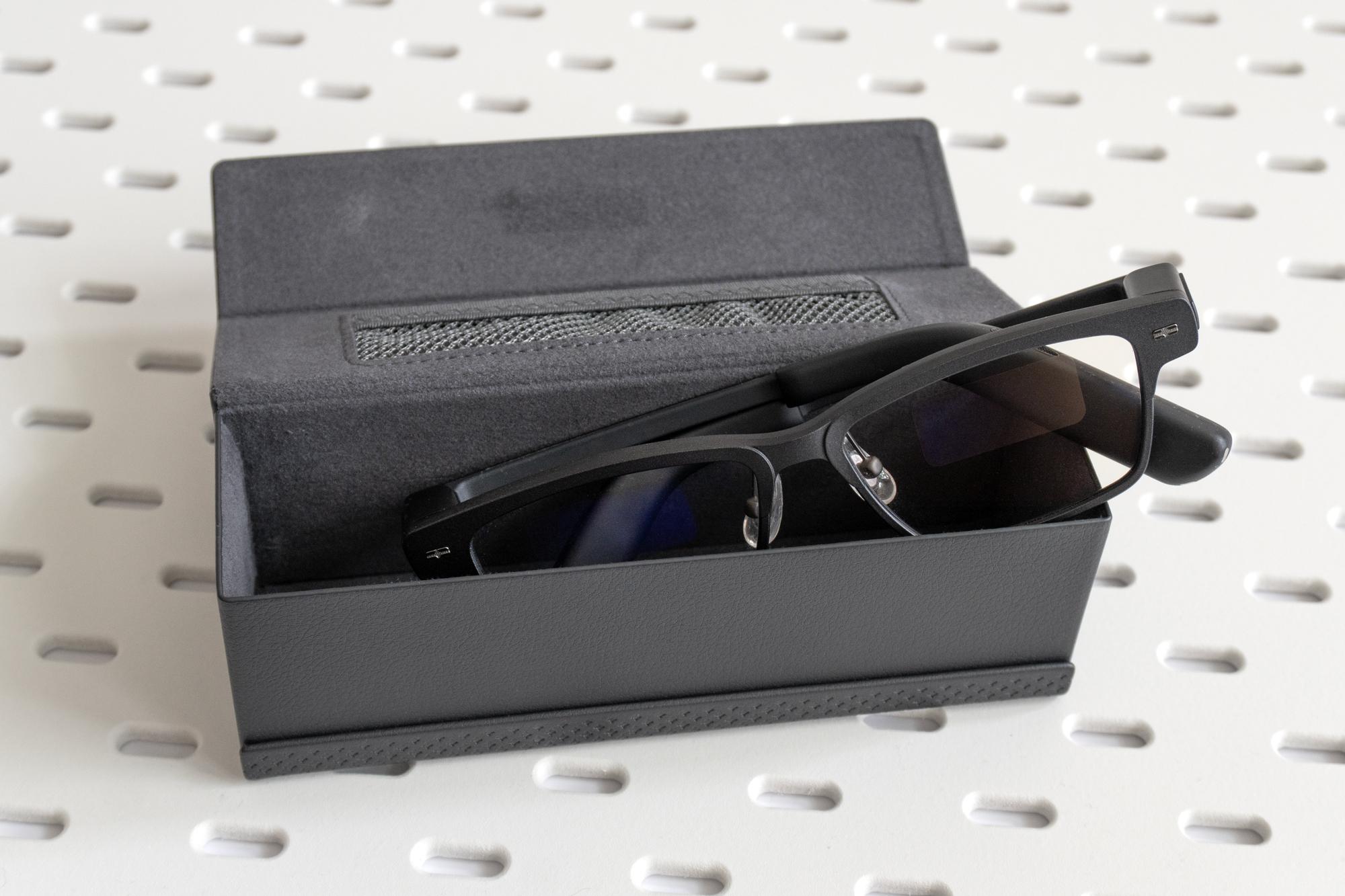 The MemoMind One smart glasses half inserted into their carrying case.