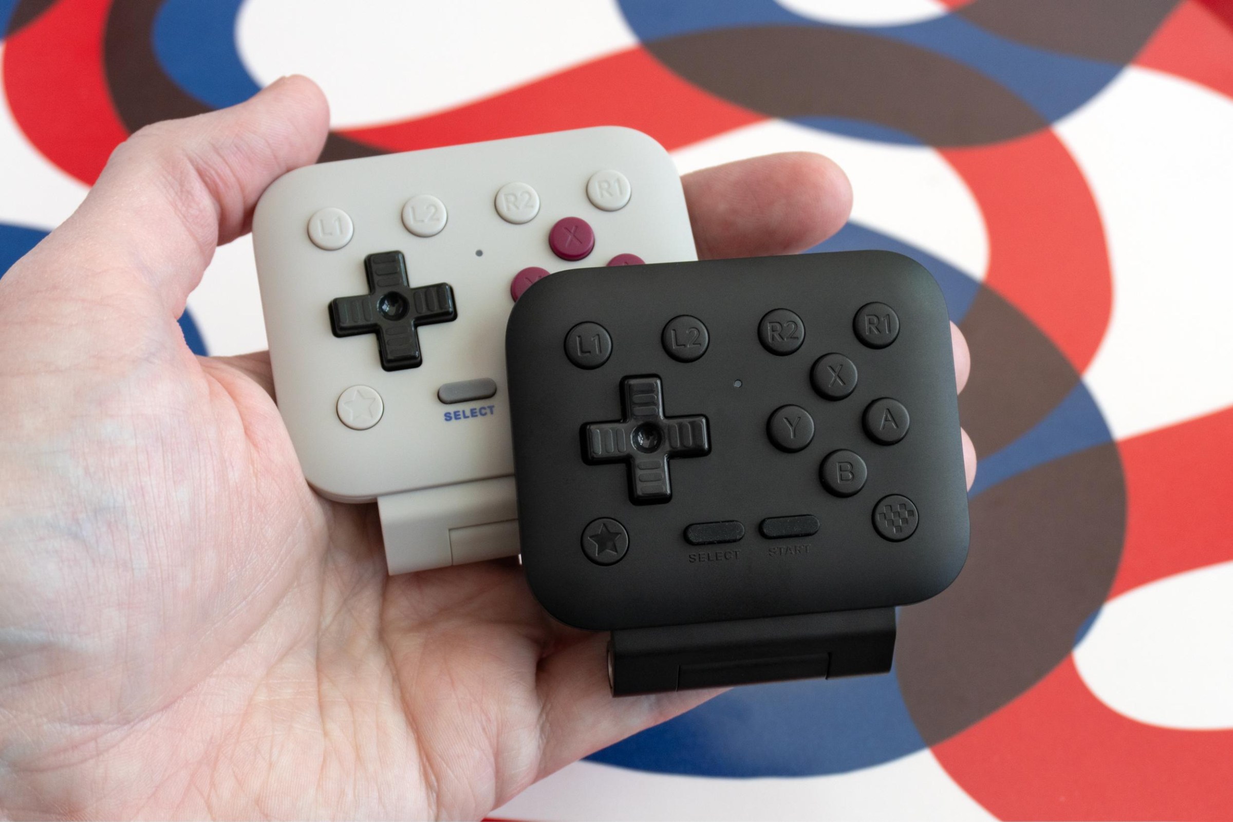 A person holding two different colored versions of the 8BitDo FlipPad.