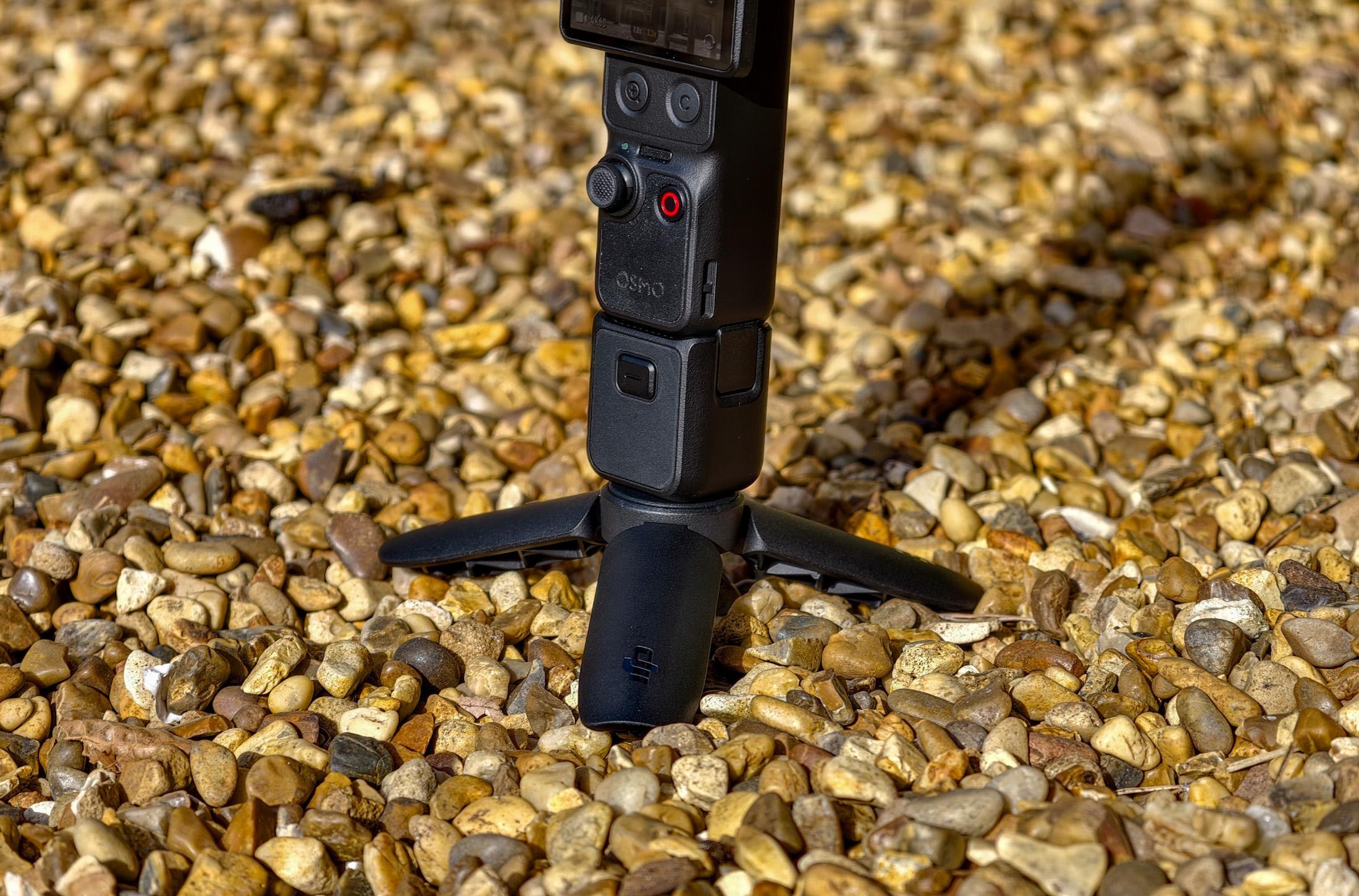 Photo of DJI Osmo Pocket 4P sitting on gravel, showing the tripod attachment.