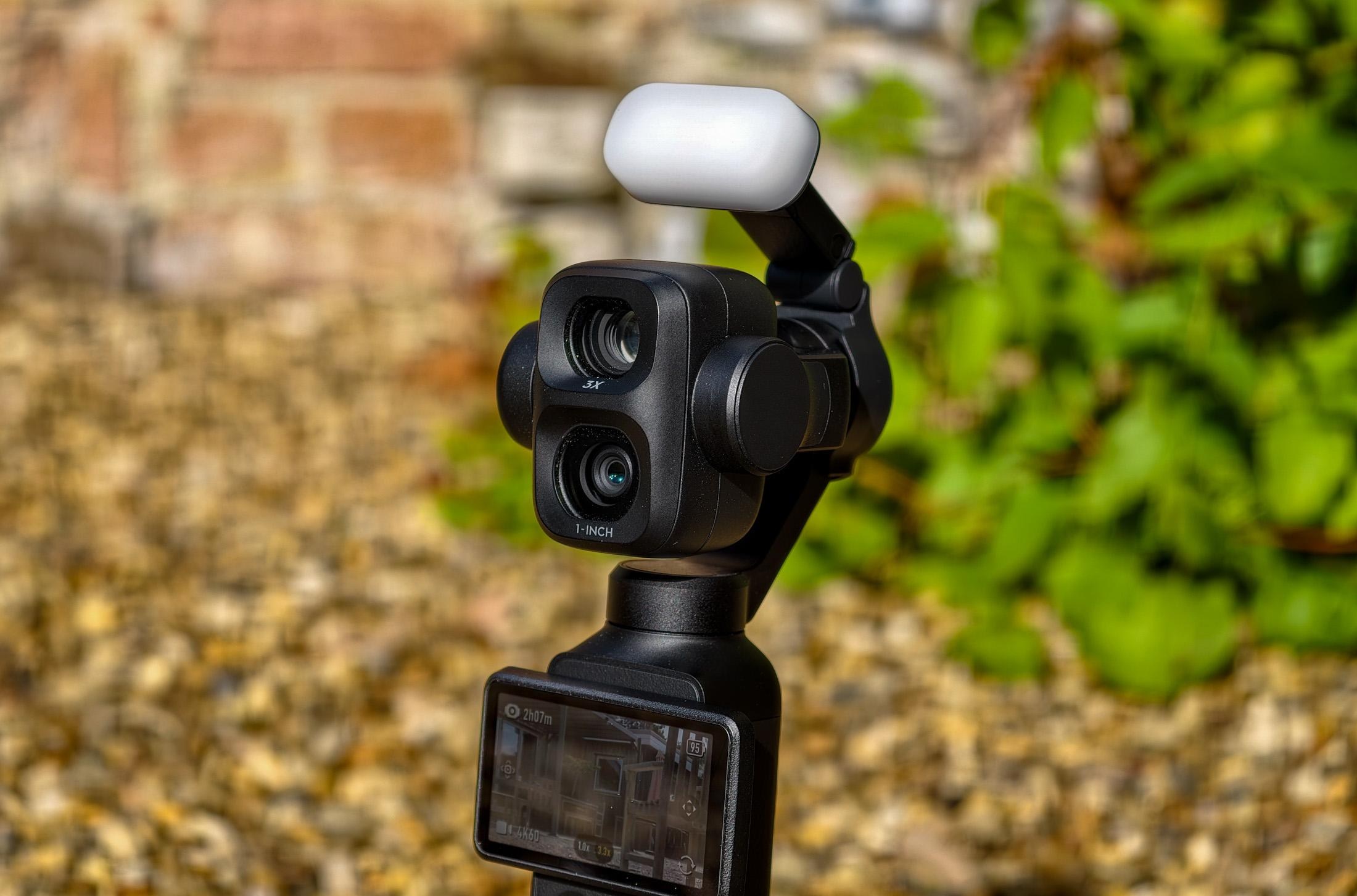 Photo of DJI Osmo Pocket 4P sitting on gravel, showing the two cameras with a lit fill light attachment above the lenses.
