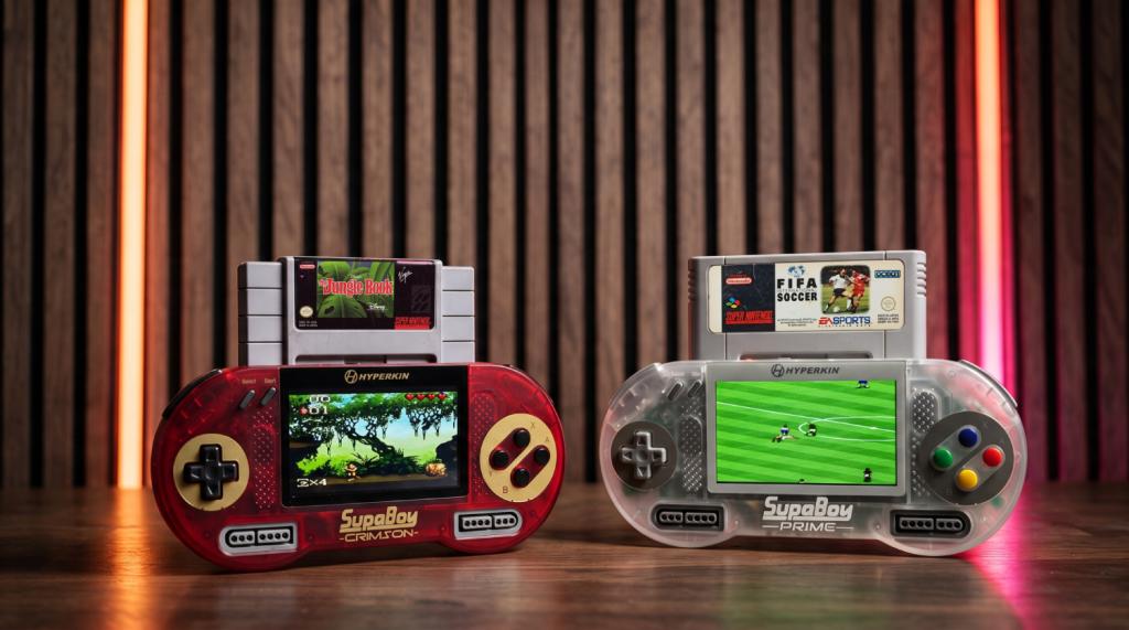 A pair of Hyperkin SupaBoy handheld consoles on a wooden surface. One is playing The Jungle Book, the other FIFA International Soccer.
