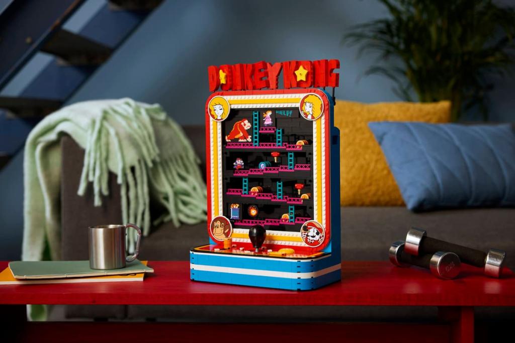 A fully assembled Lego Donkey Kong model on a table. There's a metal mug and some small dumbbells either side of it and some pillows and a blanket in the background. 
