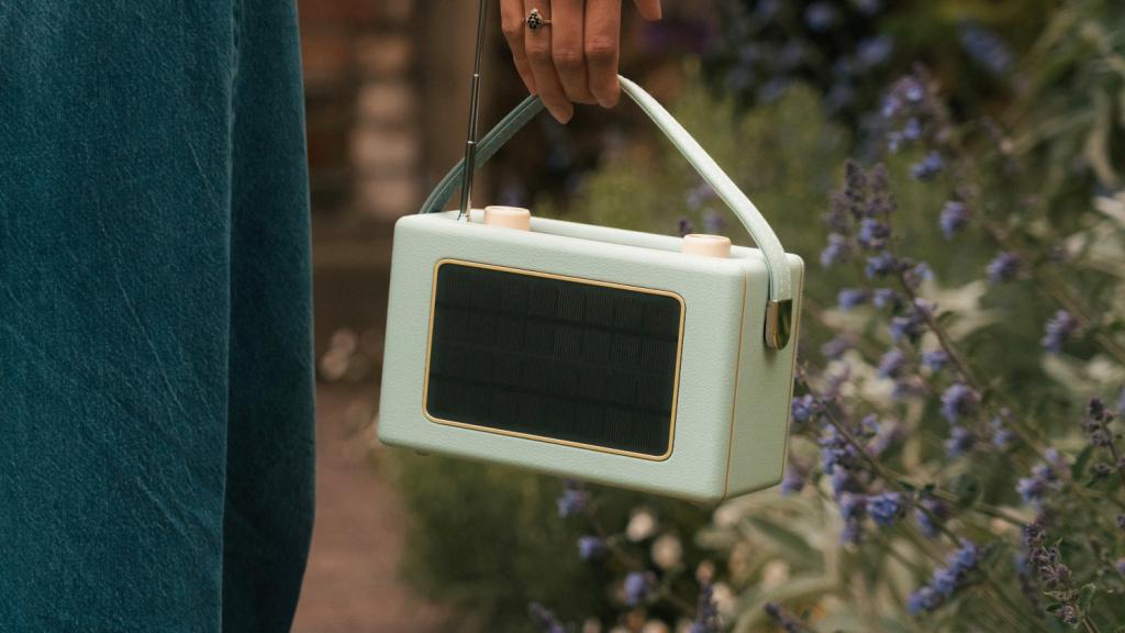 Somebody holding a light green Roberts Revival Uno Solar by the handle so that the solar panel on the back is visible.