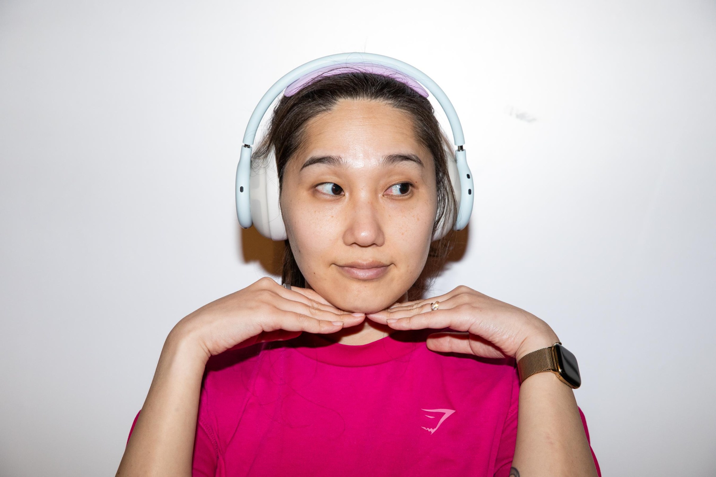 A woman wearing white Beats 360 headphones with her hands up under her chin.