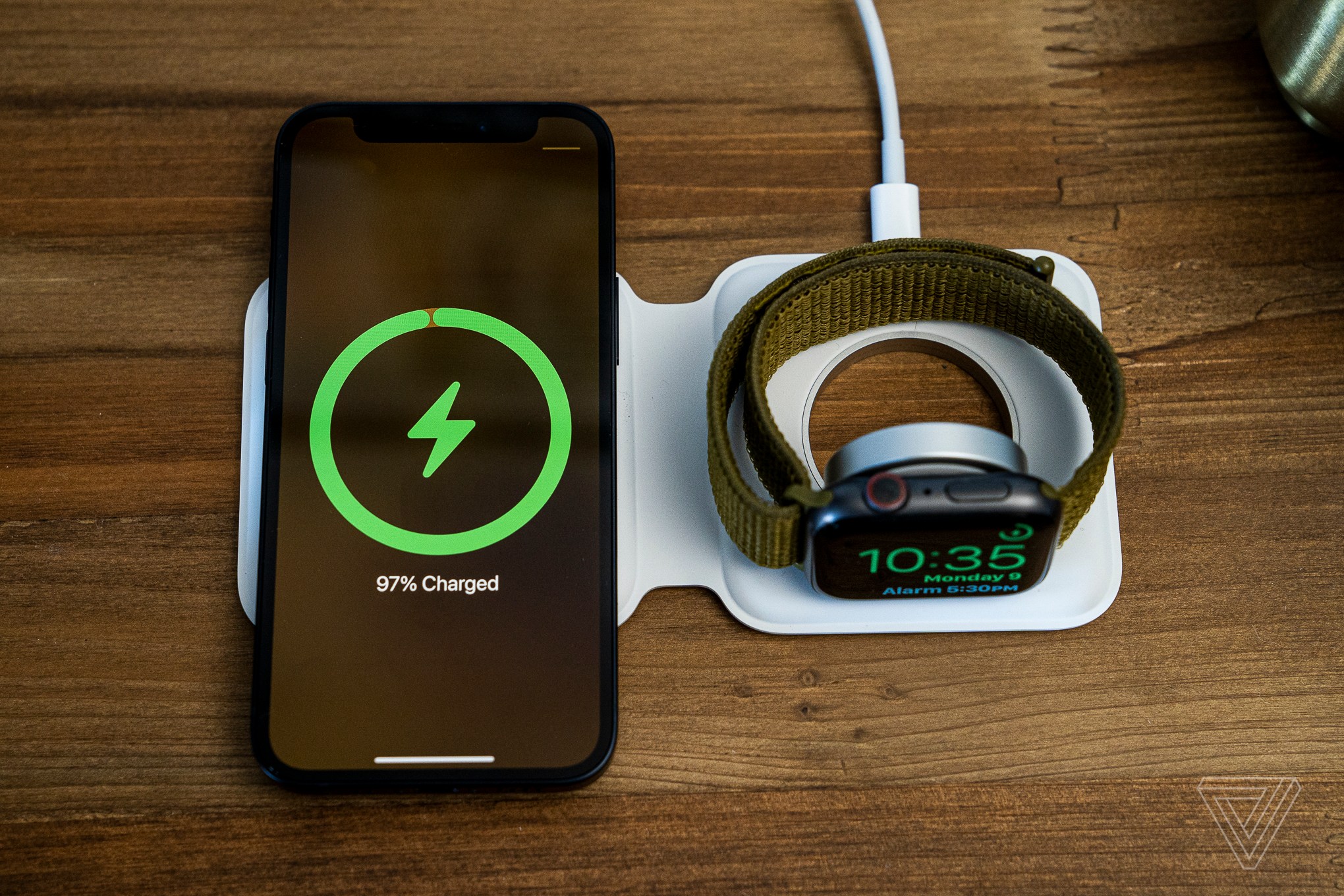 An iPhone and Apple Watch charging wirelessly on an Apple MagSafe Duo Charger, atop a wood table.